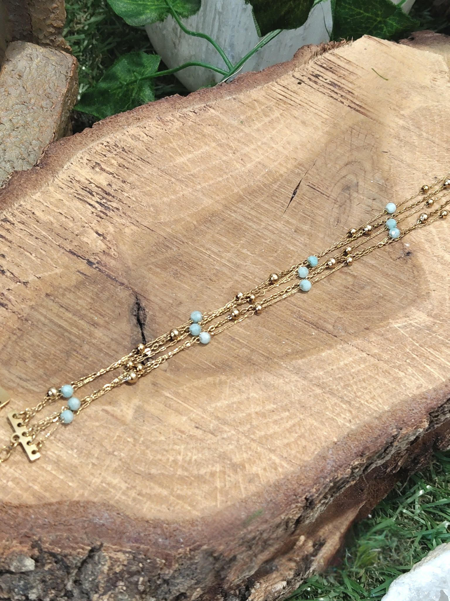 Bracelet doré en amazonite facettée posé en diagonale sur rondin en bois, bijou multi-rangs en acier inoxydable dans un décor végétal