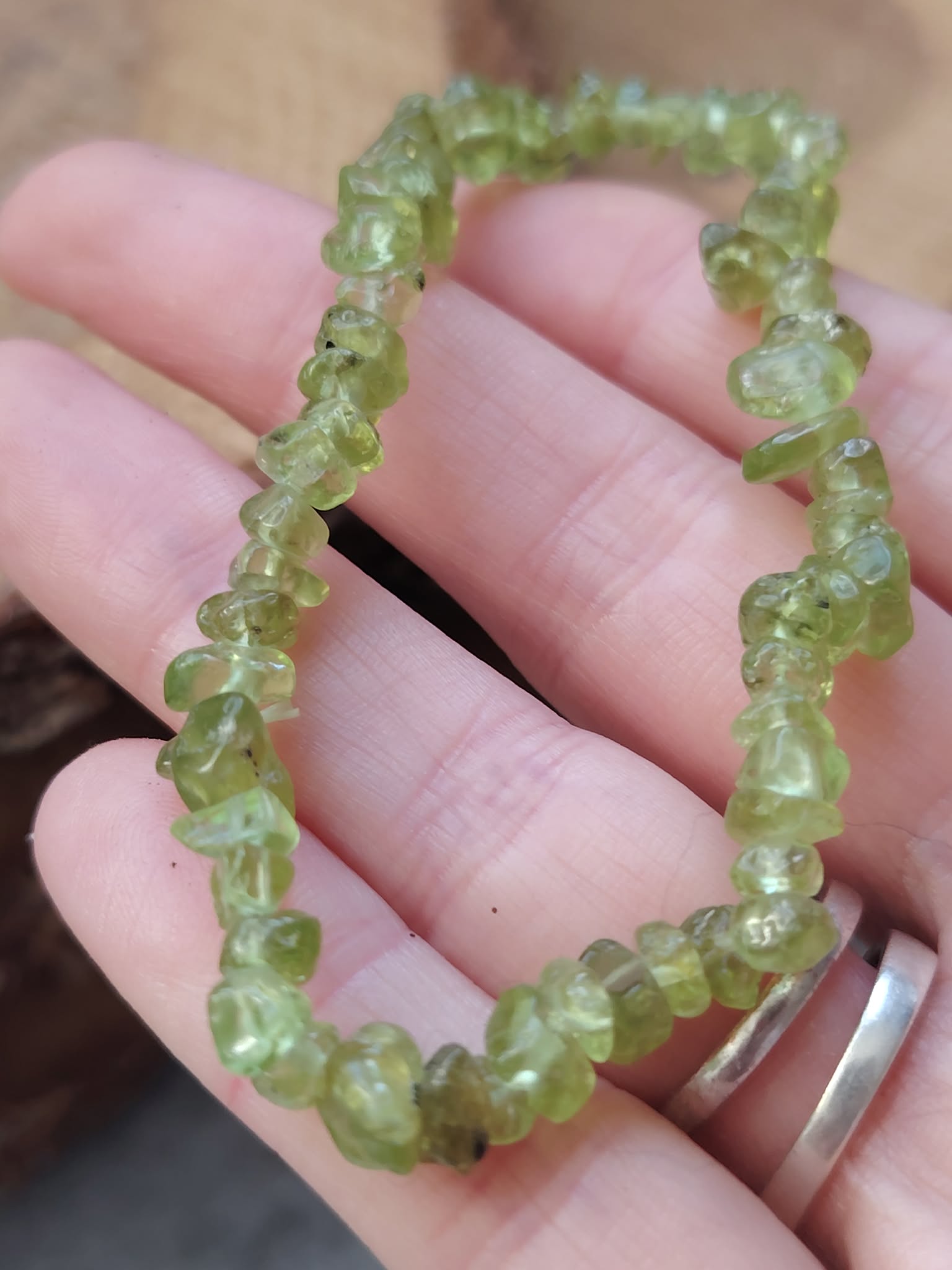 Bracelet péridot baroque tenu en main, éclats vert olive sur élastique pour clarté émotionnelle, joie tranquille et ouverture du cœur