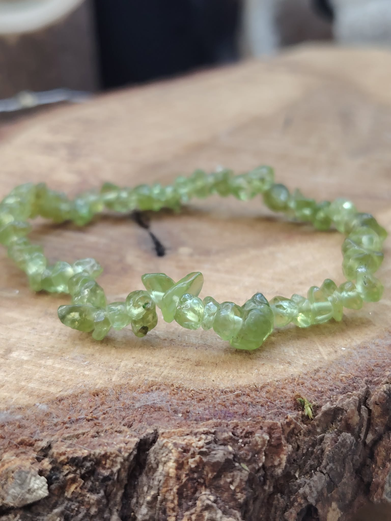Bracelet péridot baroque sur tranche de bois avec écorce visible, gros plan sur chips verts translucides pour confiance intérieure et respiration émotionnelle