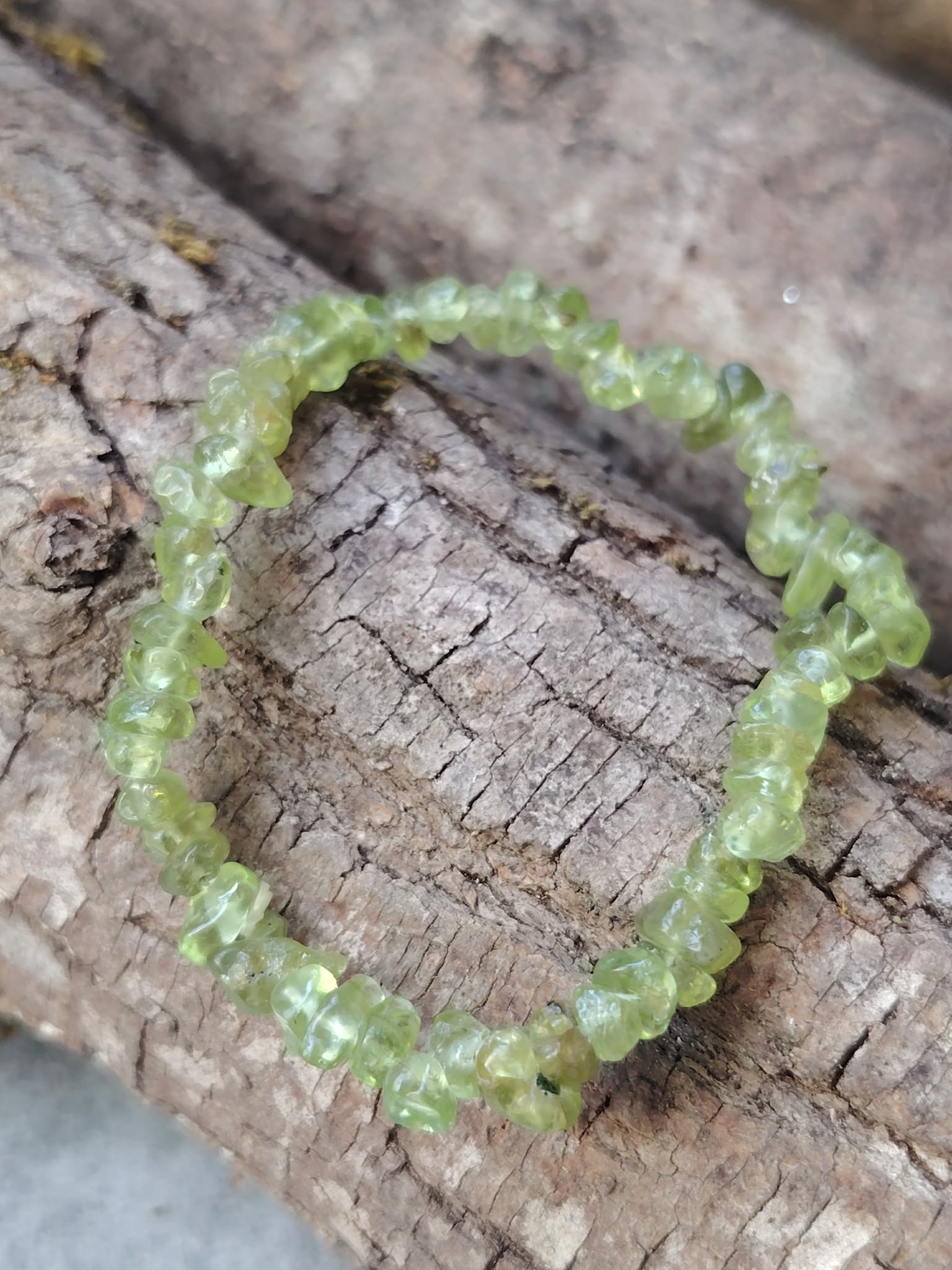 Bracelet péridot baroque sur tronc de bois veinuré en lumière naturelle, chips verts translucides pour renouveau, vitalité douce et clarté du cœur