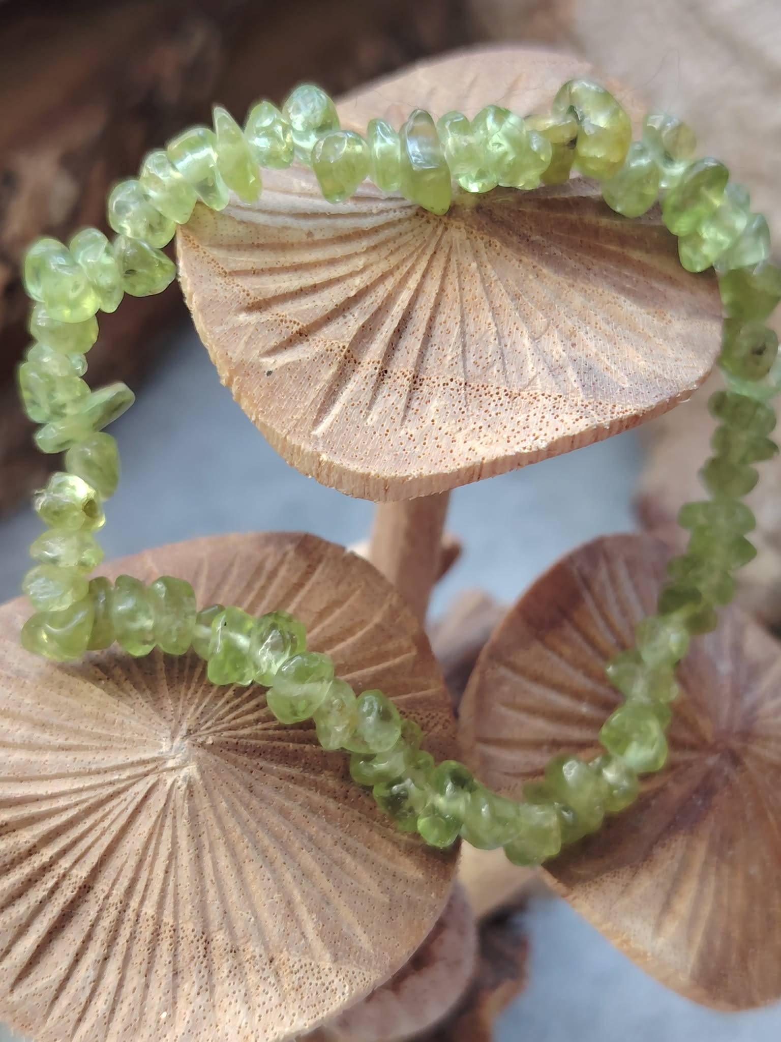 Bracelet péridot baroque en cercle sur décor champignons en bois avec fond bleu, éclats verts lumineux pour fraîcheur mentale et élan positif