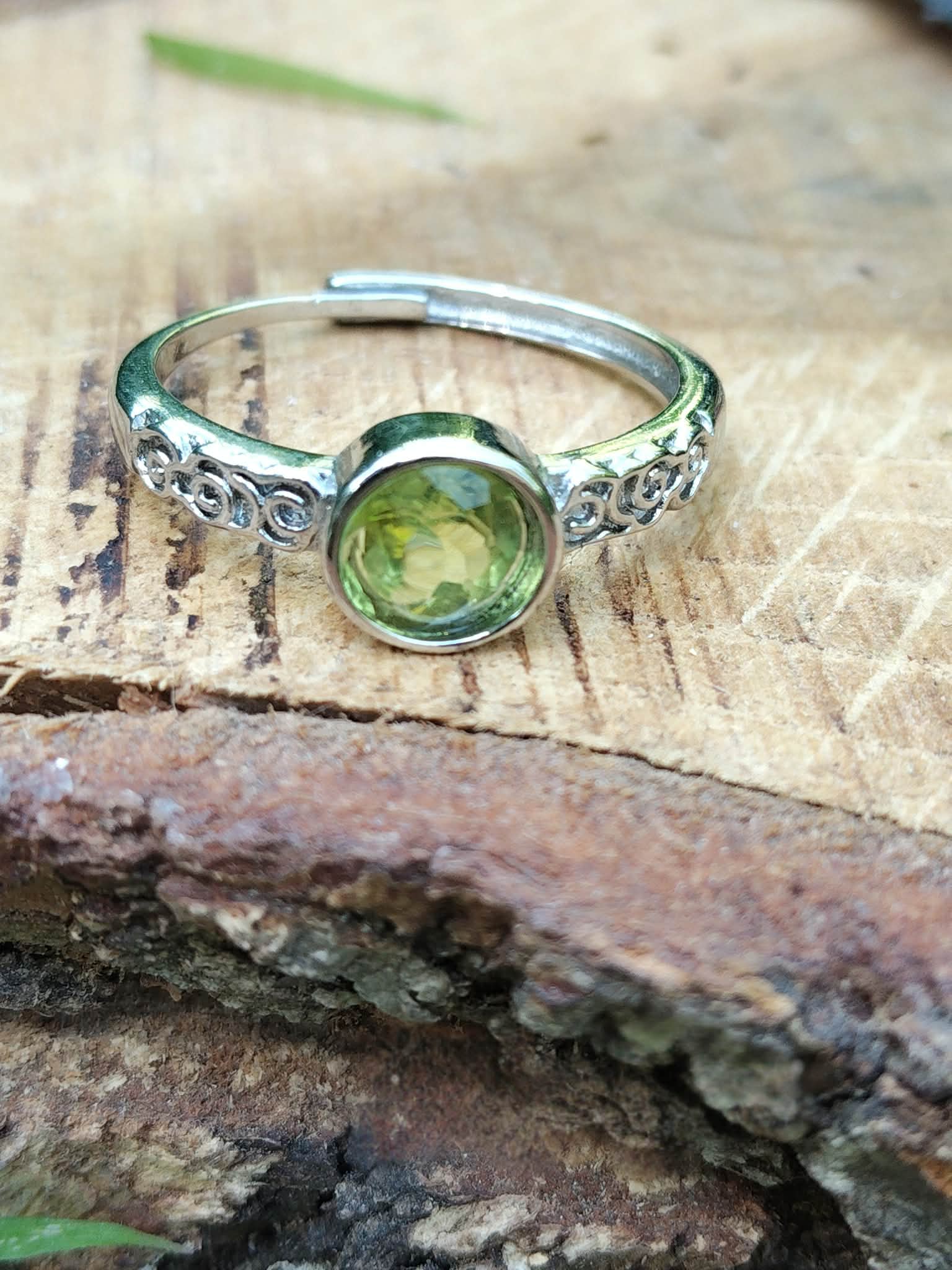 Bague péridot facetté vert olive, monture réglable, posée sur tronc texturé ; soutient la sérénité, la confiance et l’harmonie intérieure.