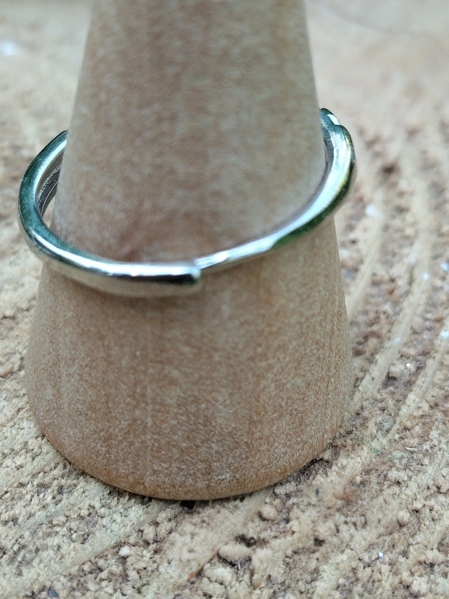 Bague réglable en cuivre blanc, vue de dos sur support en bois, posée sur rondin ; apporte apaisement, clarté et confiance.