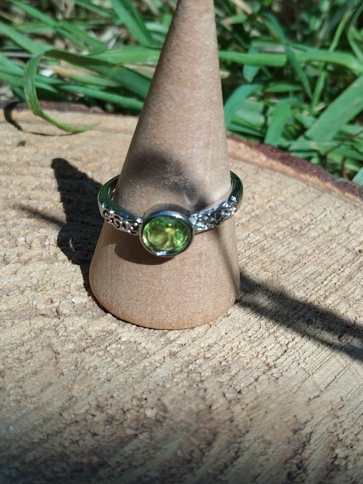 Bague réglable en cuivre blanc, péridot facetté lumineux, mise en scène sur support beige et bois ; encourage confiance et énergie positive.