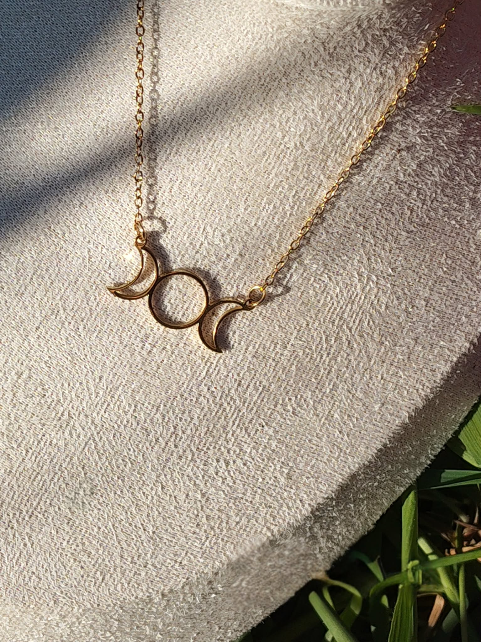 Collier triple lune doré porté sur buste beige en extérieur avec herbes en fond, bijou lunaire en acier inoxydable
