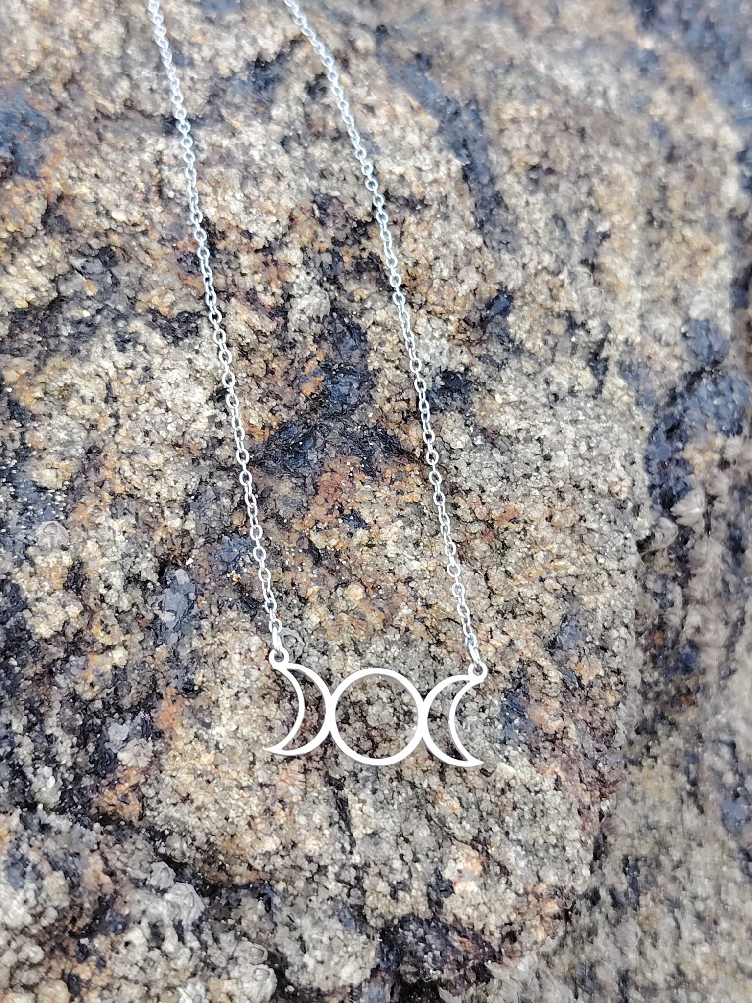 Collier triple lune en acier inoxydable sur rocher granit en extérieur, symbole lunaire au style mystique photographié en Bretagne