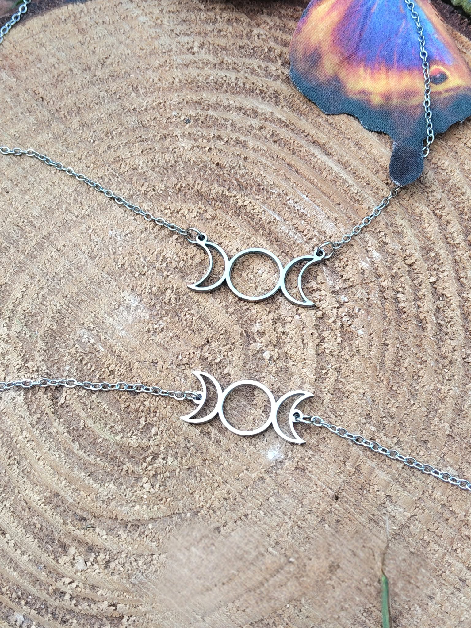 Pendentif et bracelet triple lune dorés posés sur une tranche de bois avec reflets multicolores, duo de bijoux symboliques