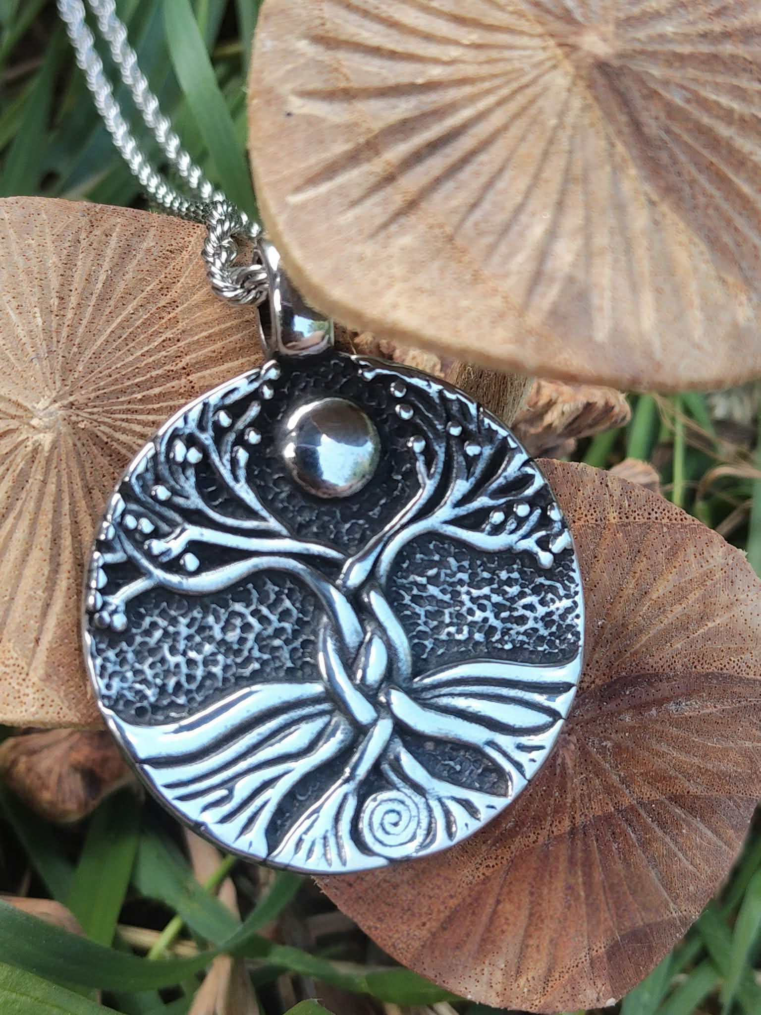 Pendentif Yggdrasil argenté sur chaîne, posé sur champignons en bois et herbe, bijou symbolique d’ancrage et d’élan vital