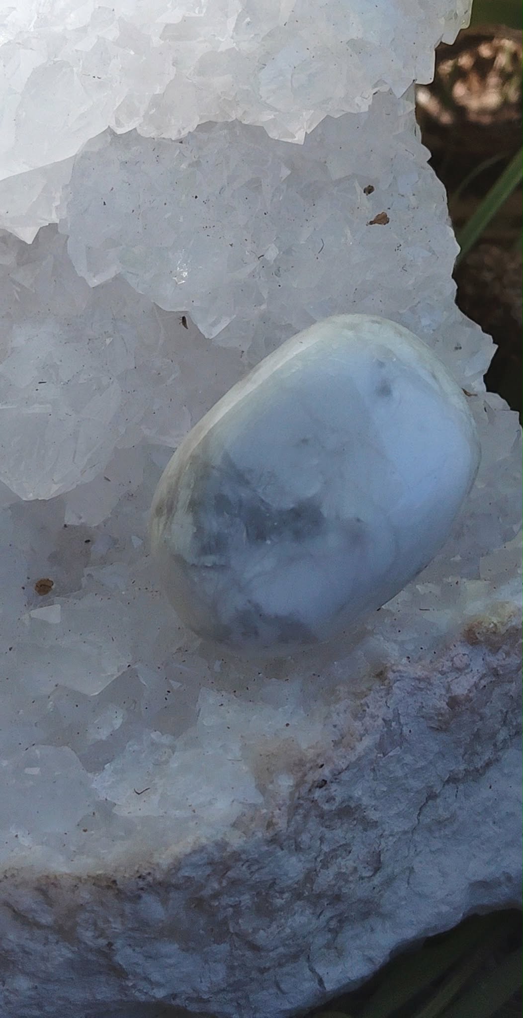 Pierre roulée howlite blanche marbrée de gris posée dans une géode claire, cristaux blancs et gris en lumière tamisée, pierre naturelle associée à l’intuition douce, au calme intérieur et à la clarté mentale.