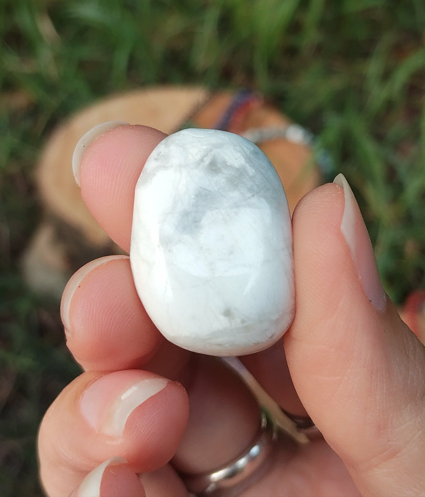 Pierre roulée howlite blanche veinée de gris tenue entre les doigts, décor végétal flouté en arrière-plan, pierre naturelle évoquant la douceur émotionnelle, la communication apaisée et le recentrage.