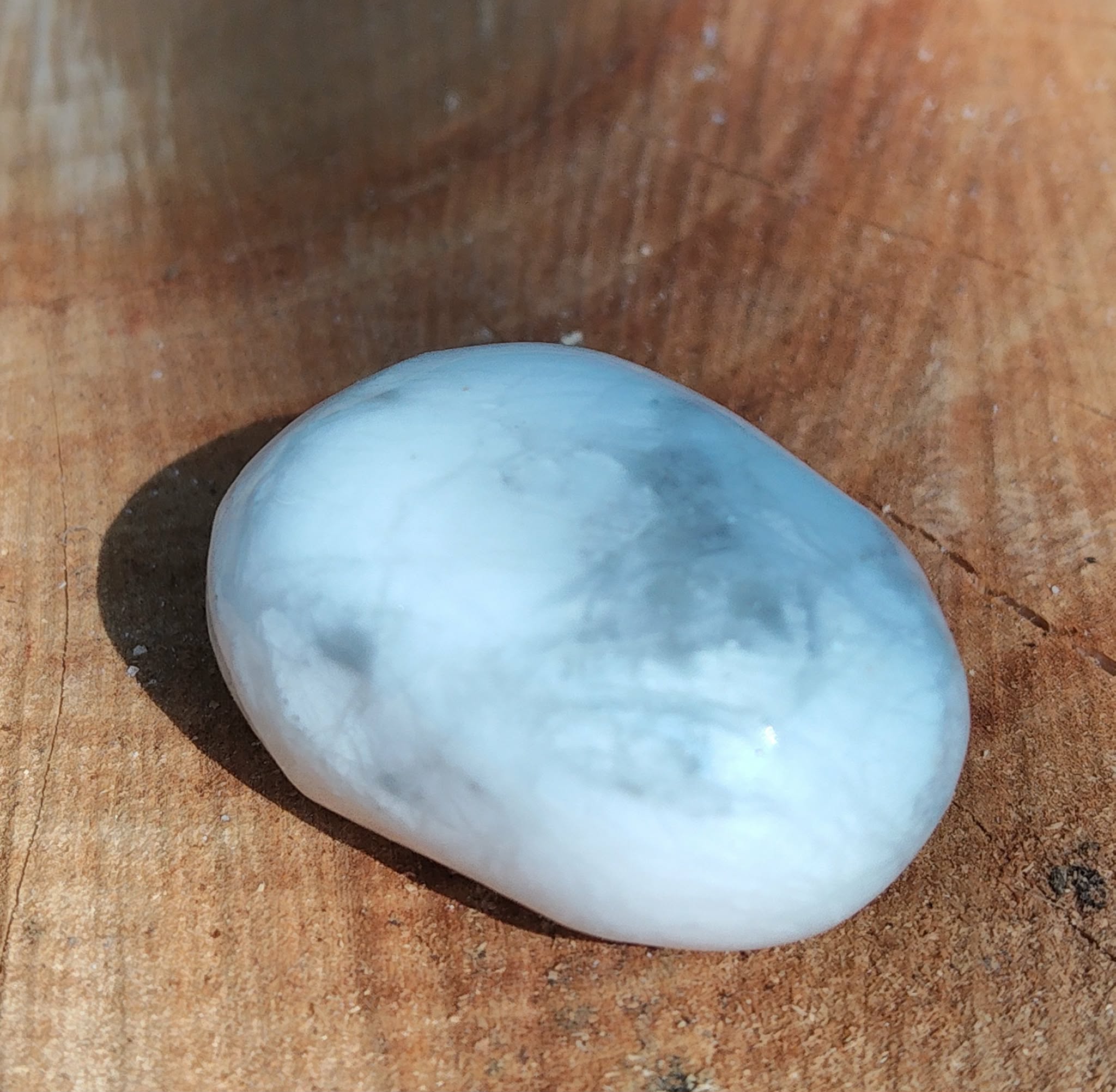 Pierre roulée howlite blanche marbrée de gris polie sur tranche de bois, reflets doux et veinures nuagées, pierre naturelle associée à la tranquillité, à la justesse d’expression et à la lucidité.