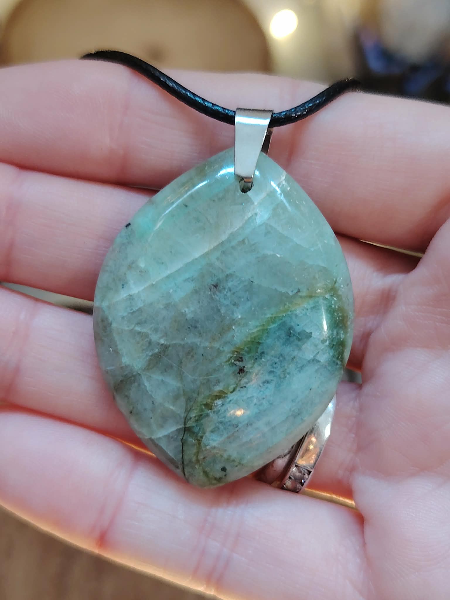 Pendentif en garniérite verte sur cordon noir, tenu en main avec pierre polie facettée et bélière argentée, pierre naturelle associée à la lucidité, à l’apaisement et à la confiance intérieure.