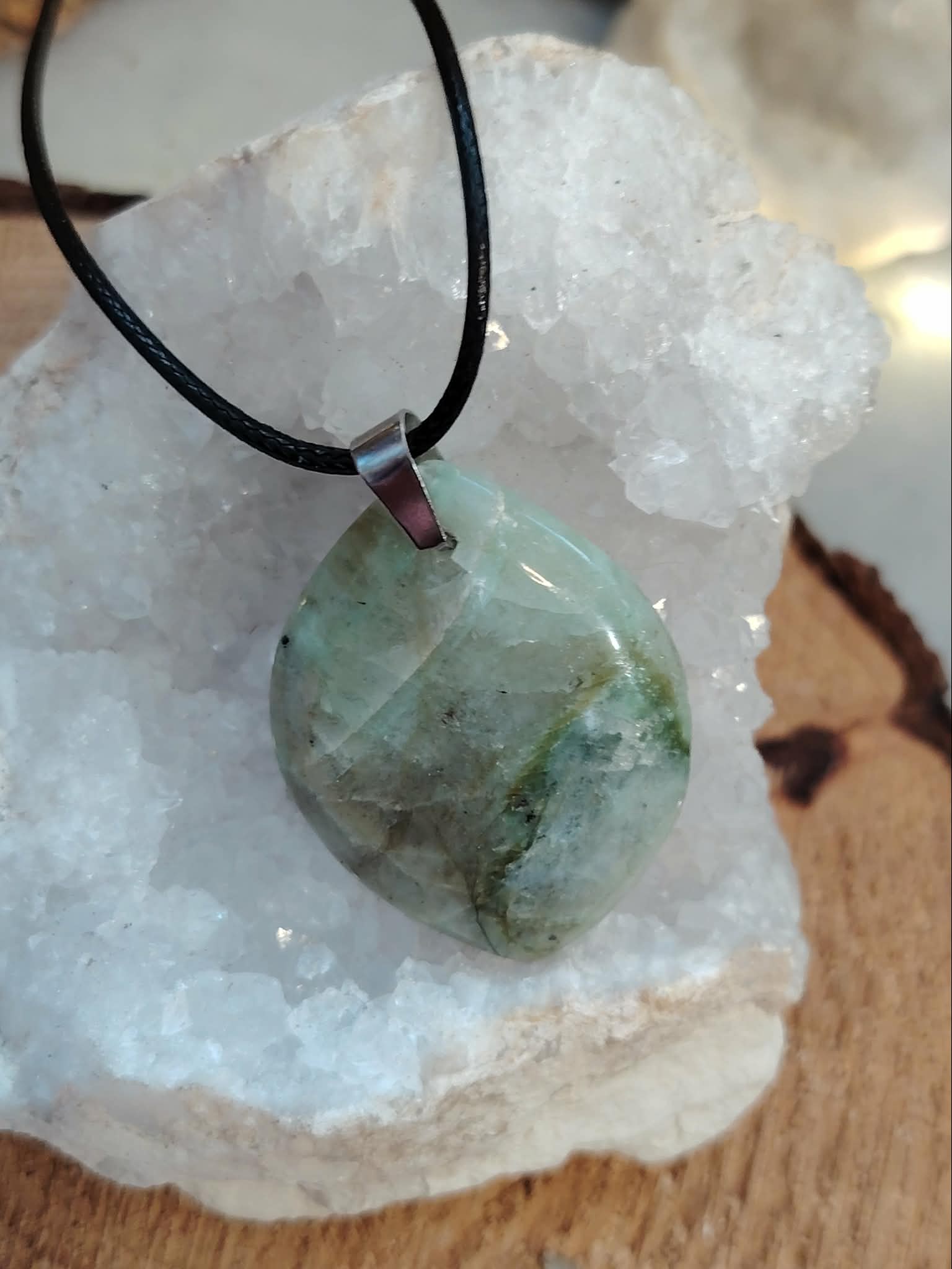 Pendentif en garniérite vert d’eau sur cordon noir, pierre polie posée sur géode blanche en décor minéral, pierre naturelle liée au réconfort émotionnel, au recentrage et à la tranquillité intérieure.