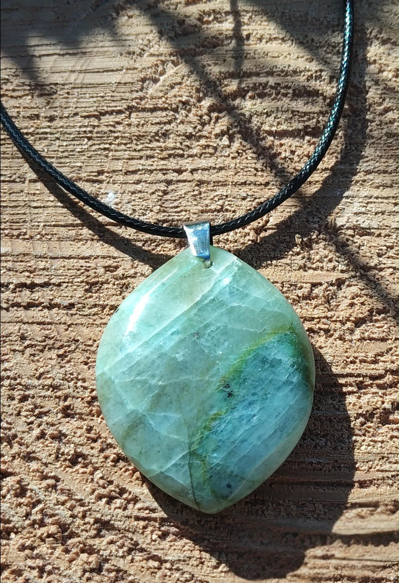Pendentif en garniérite vert d’eau sur cordon noir, pierre polie marbrée posée sur bois brut, bijou en pierre naturelle associé à la stabilité, au calme du mental et à la présence à soi.