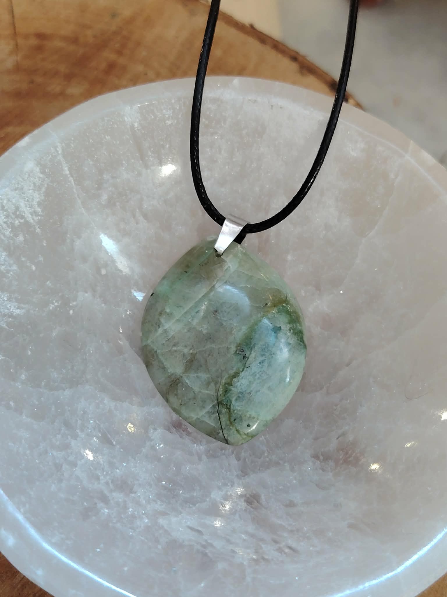 Pendentif garniérite verte sur cordon noir avec bélière argentée, posé sur une géode de quartz blanc, pierre naturelle reliée au calme intérieur, à la finesse émotionnelle et à l’ancrage.