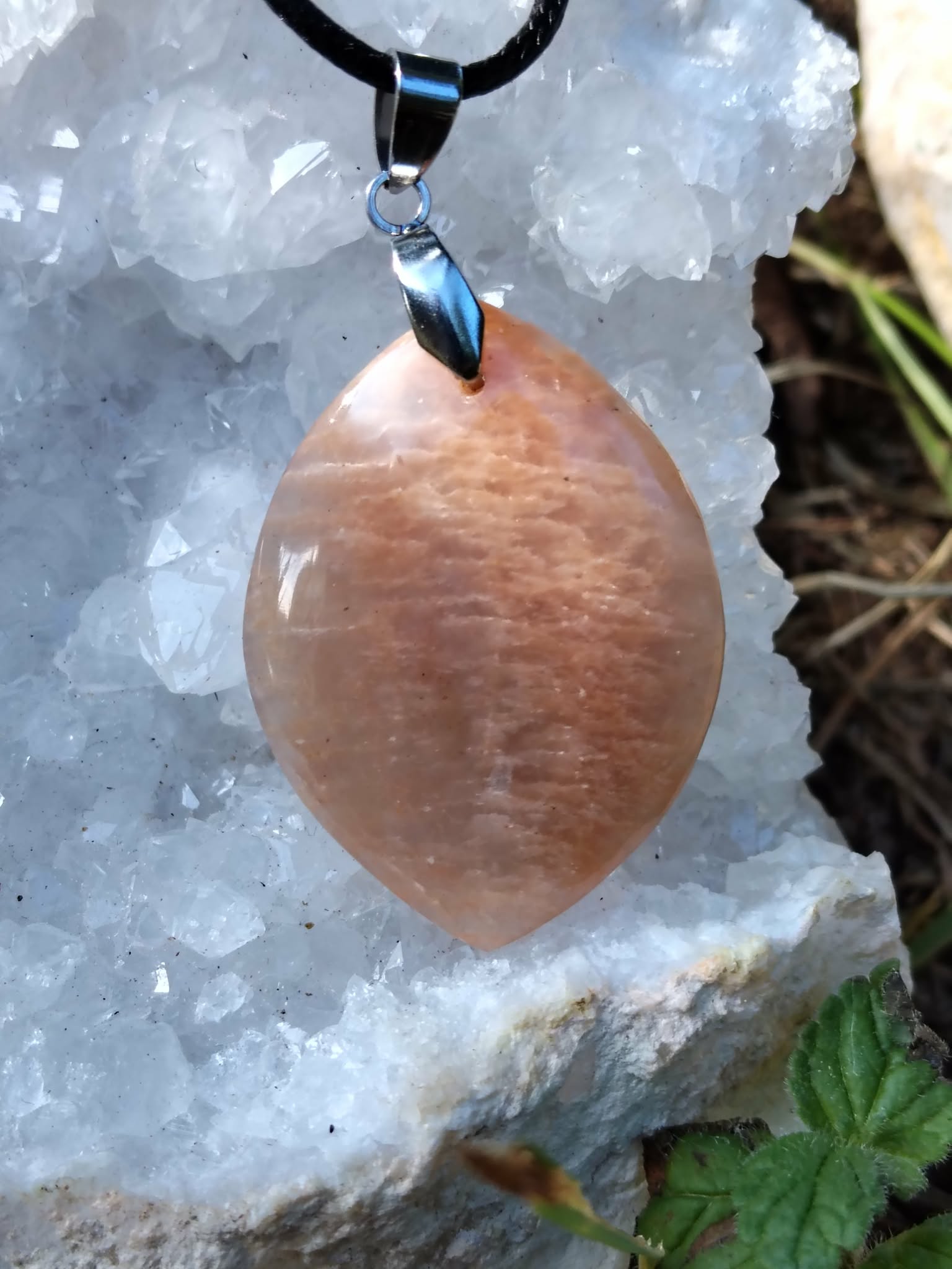 Pendentif goutte en pierre de soleil sur cordon noir, posé sur cristaux blancs et mousse, bijou en pierre naturelle associé à la chaleur intérieure, à l’élan positif et à la confiance douce.