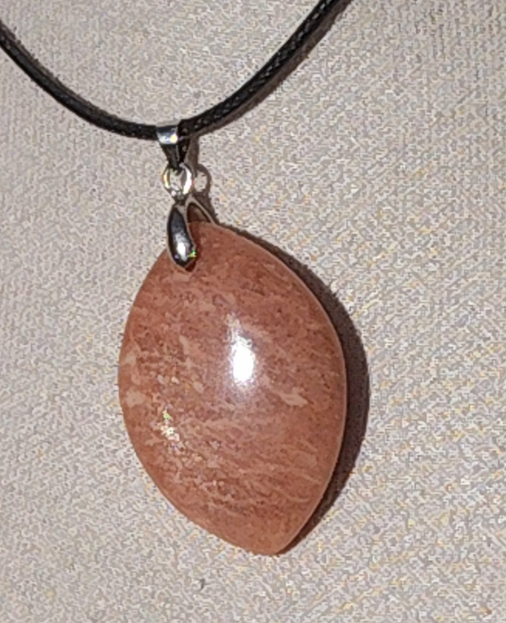 Pendentif goutte en pierre de soleil pailletée avec bélière métal sur cordon noir, fond gris, pierre naturelle évoquant l’élan solaire, la présence à soi et la confiance lumineuse.