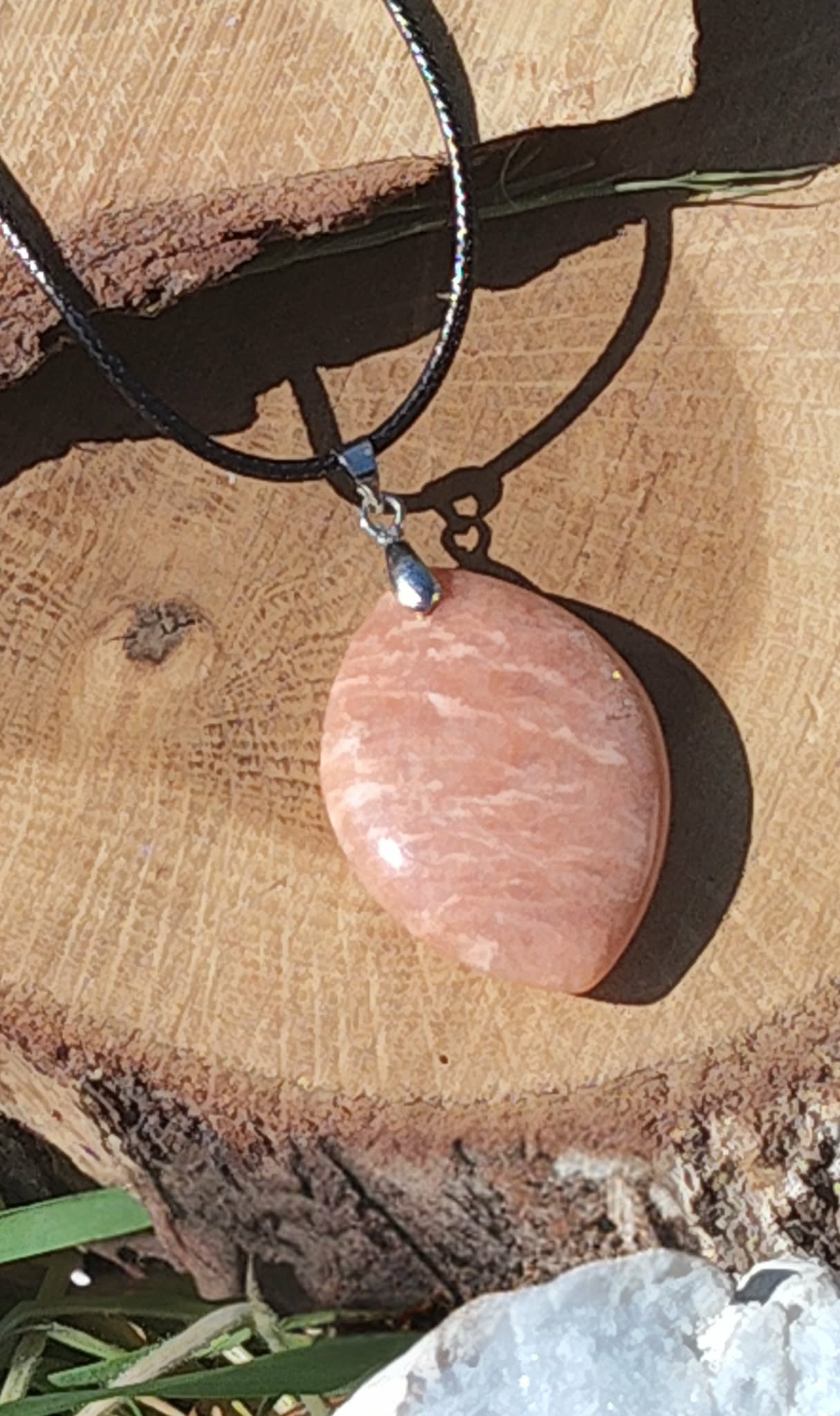 Pendentif goutte en pierre de soleil sur cordon noir, posé sur tranche de bois avec cristaux, bijou en pierre naturelle évoquant l’enthousiasme, la volonté et la lumière intérieure.