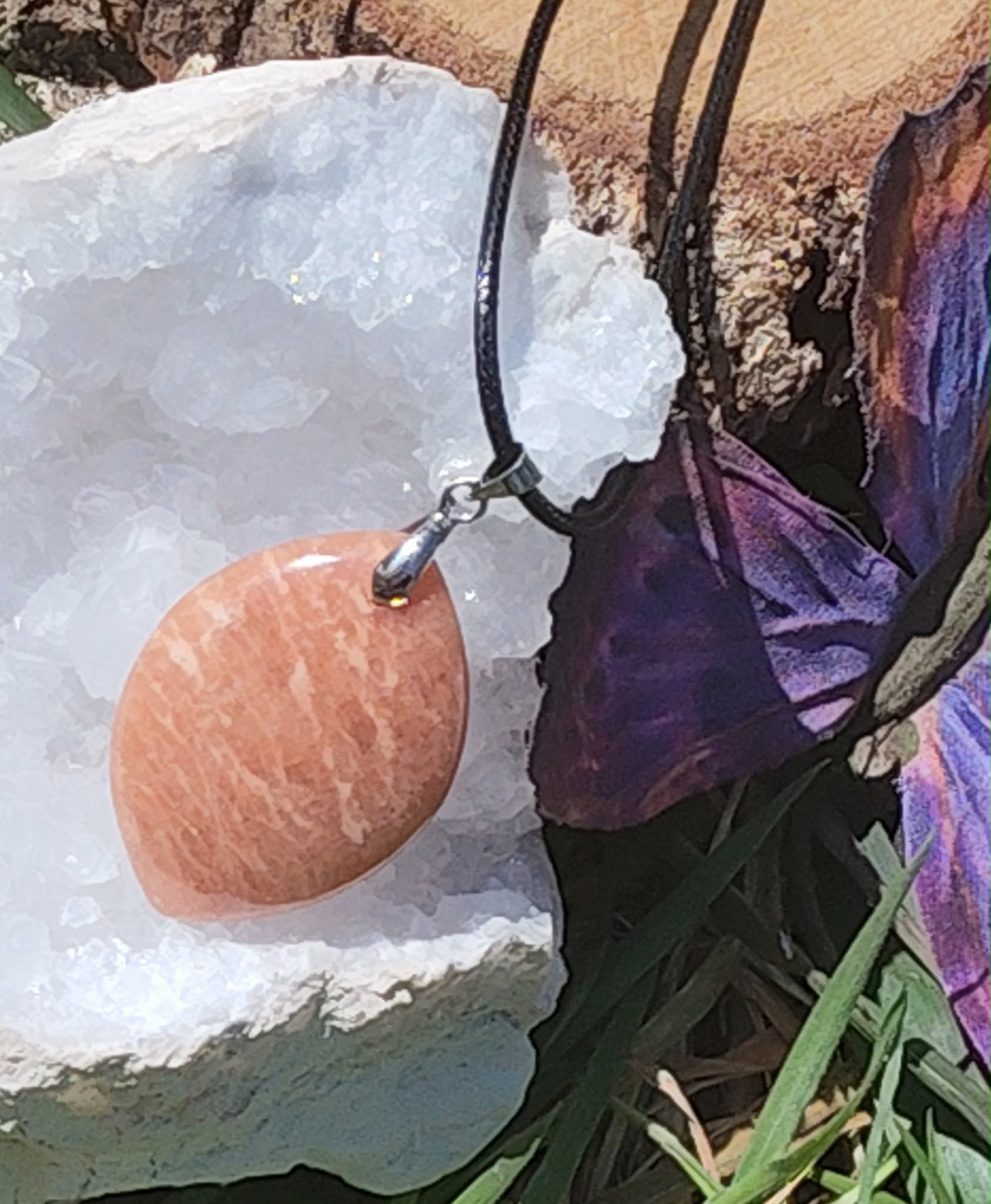 Pendentif rond en pierre de soleil sur cordon noir, posé près de cristaux blancs et décor violet, bijou en pierre naturelle lié à la bonne humeur, au dynamisme et à l’équilibre intérieur