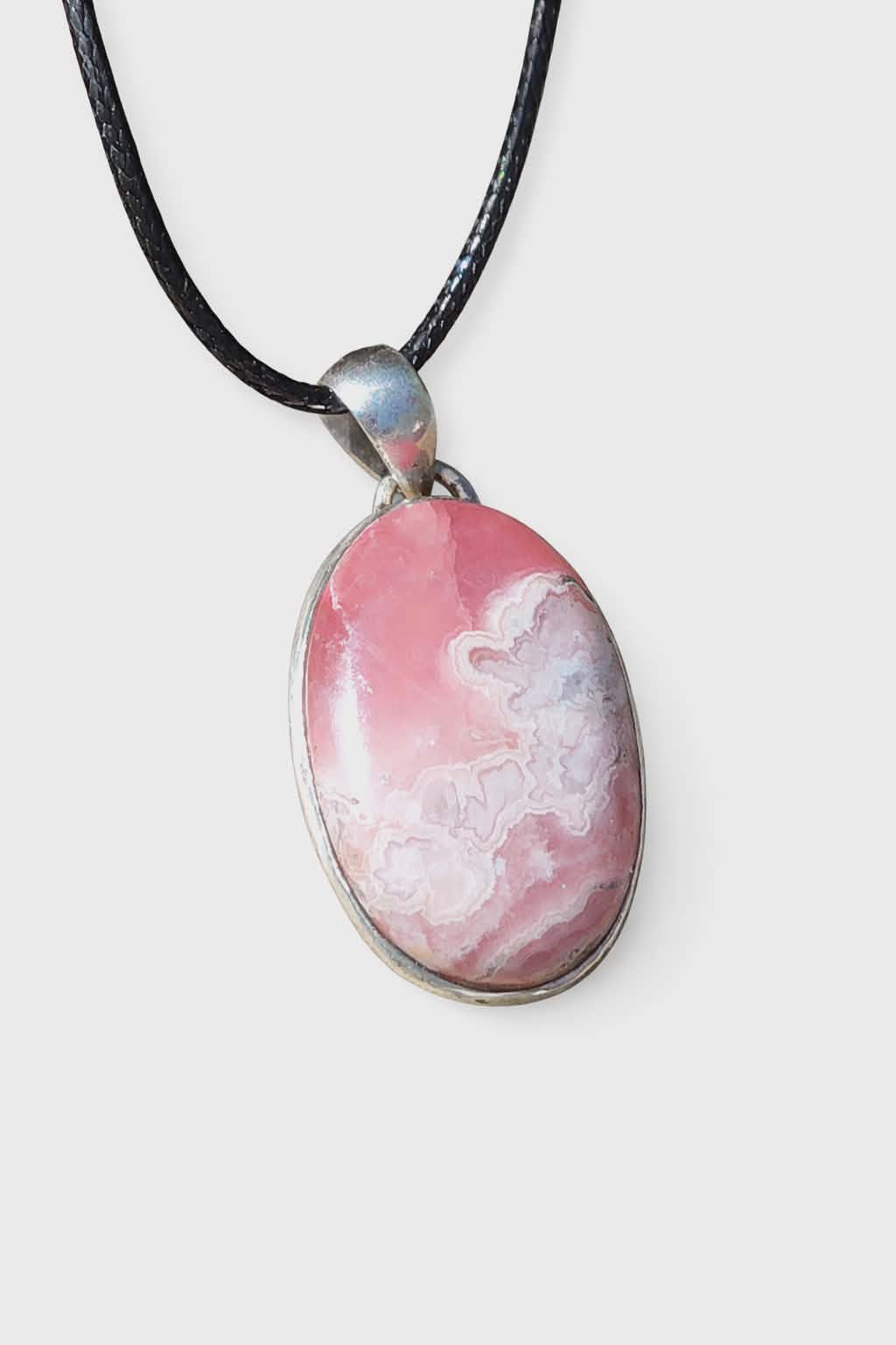 Pendentif rhodochrosite ovale rose marbré en argent 925 sur cordon noir, présenté sur fond blanc, pierre naturelle reliée à la douceur intérieure, à la paix du cœur et à la sérénité.