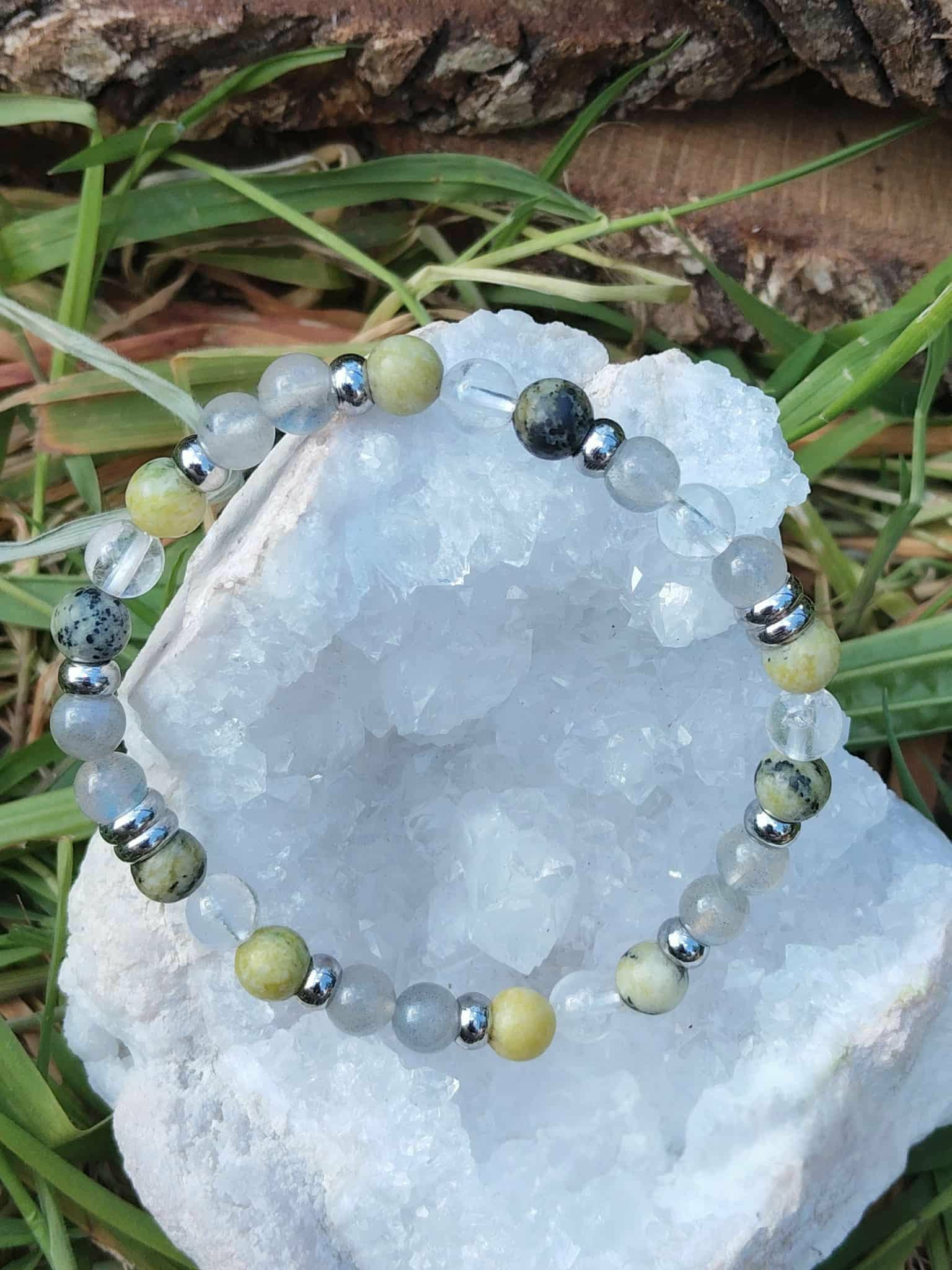 Bracelet vampire énergétique posé sur amas de quartz avec herbes en arrière-plan, trio labradorite, serpentine et cristal de roche pour nettoyage subtil et respiration mentale