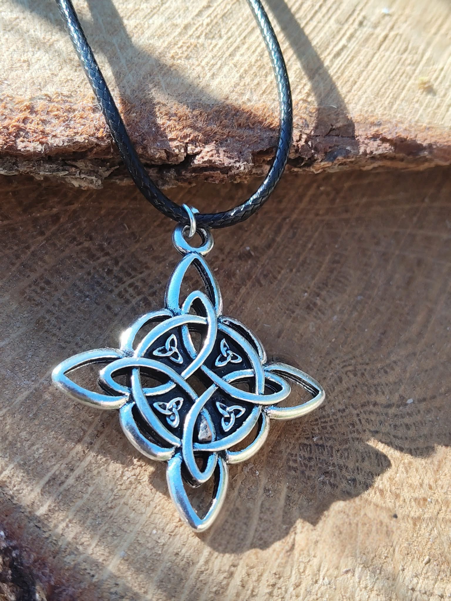 Collier avec pendentif nœud de sorcière photographié en Bretagne, symbole celtique argenté sur cordon noir pour protection et lien spirituel