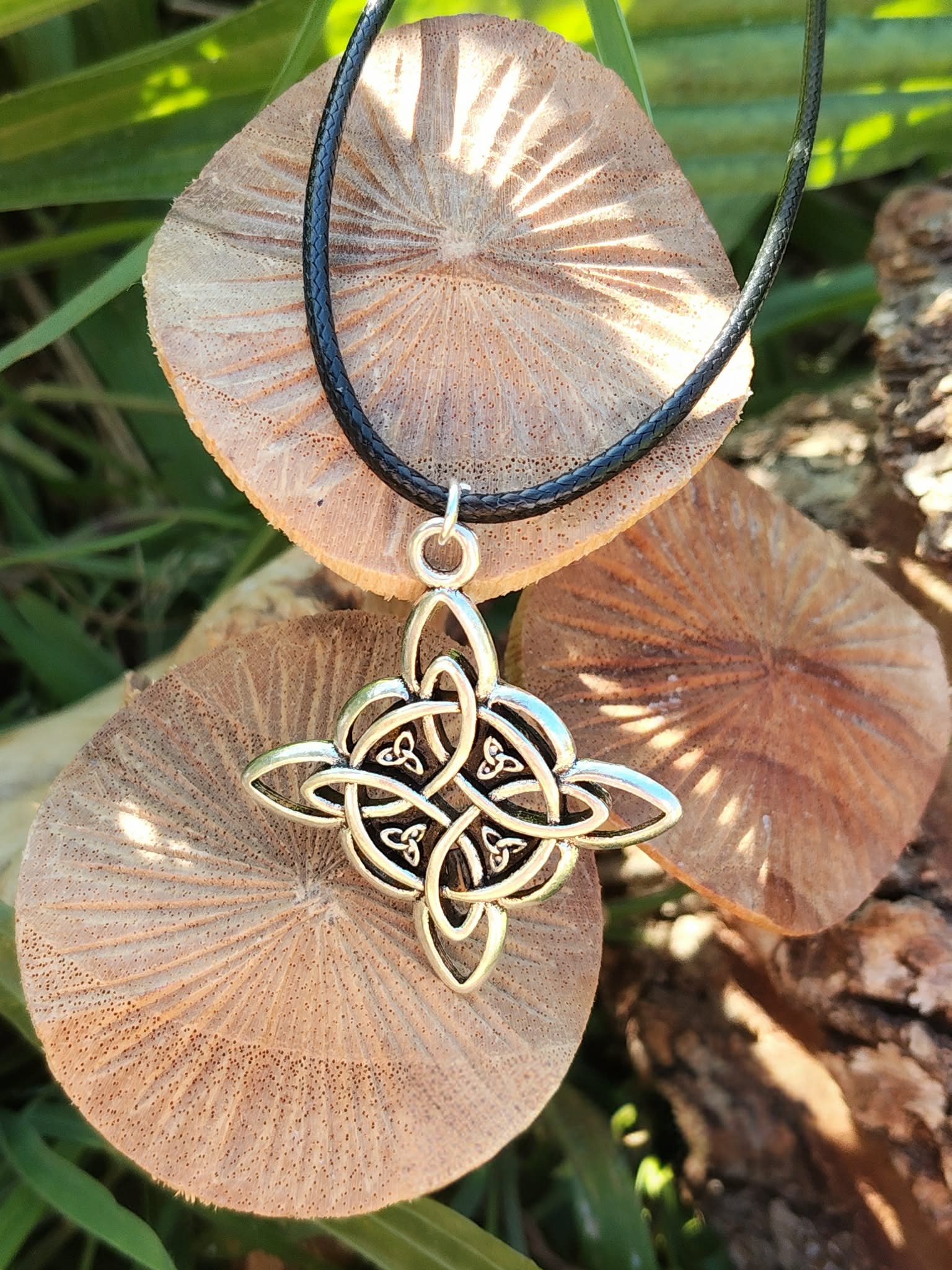 Collier sur cordon noir avec pendentif nœud de sorcière argenté, décor champignons et feuillage en lumière naturelle, harmonie et protection