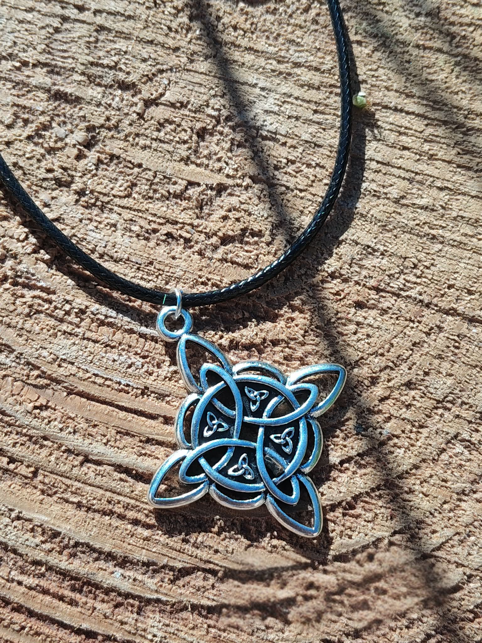 Collier cordon noir avec pendentif nœud de sorcière argenté sur rondelle de bois nervurée, lumière douce et ancrage symbolique