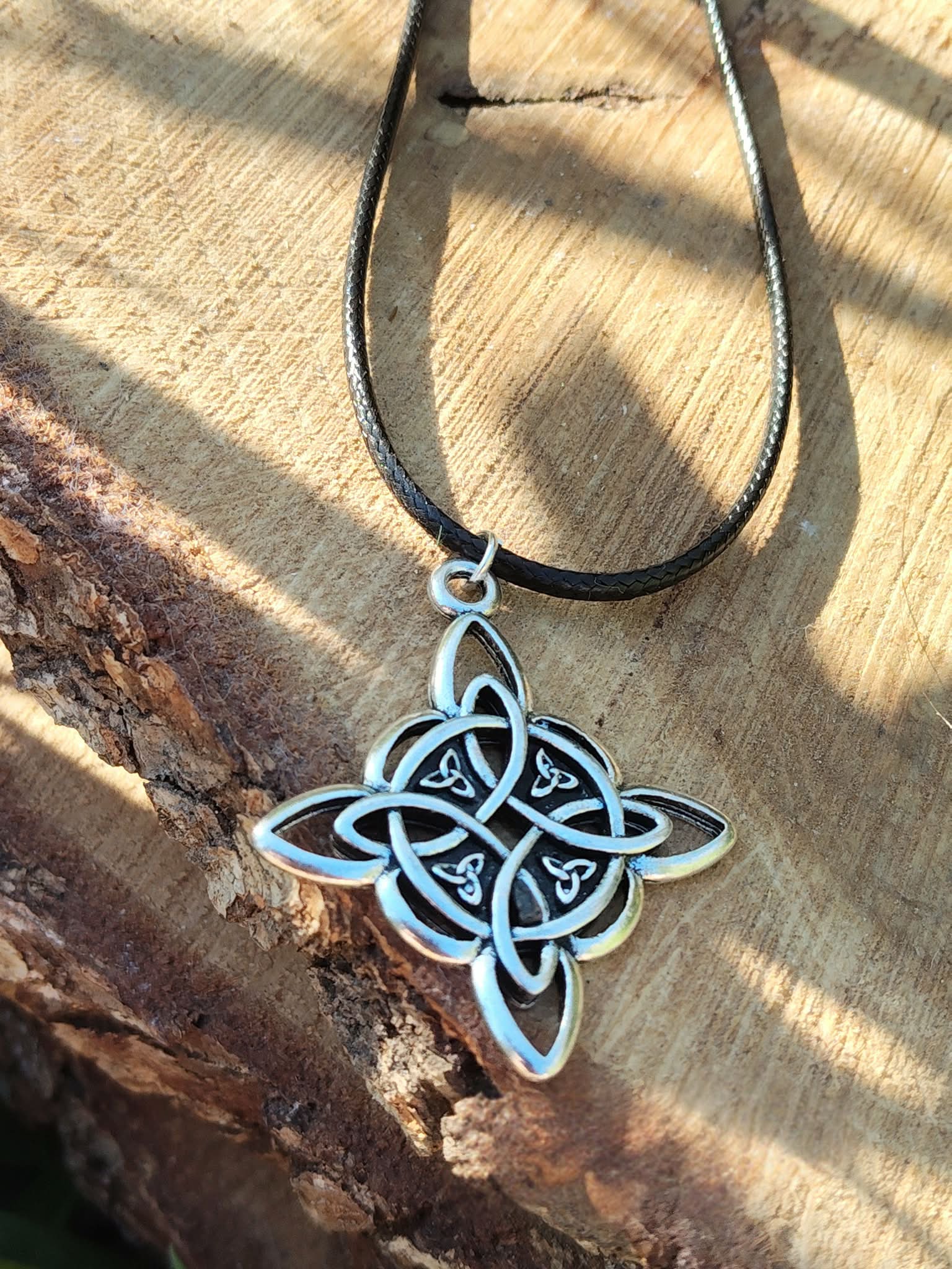 Collier nœud de sorcière argenté sur cordon noir, décor écorce et bois texturé, lumière chaude et symbole d’union continue