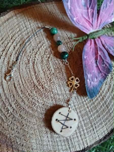 Bijou de rétroviseur witch, sigil de chance gravé, perles vertes et pêche, trèfle cuivre, cordon noir, présenté sur rondin de bois. Création Magic Gaïa