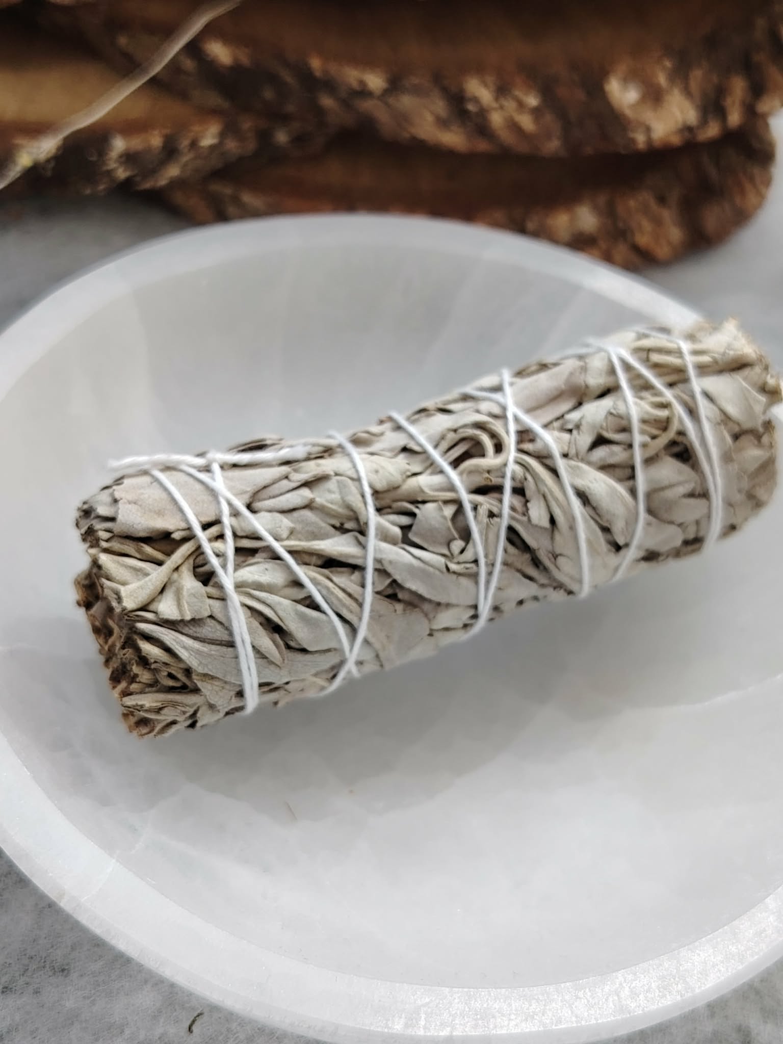 Bâton de sauge blanche à brûler (smudge) ficelé, posé sur bol en céramique blanc, fond sombre et bois. Accessoire pour fumigation, rituel, méditation, yoga, purification énergétique, nettoyage des lieux, protection, clarté et apaisement.