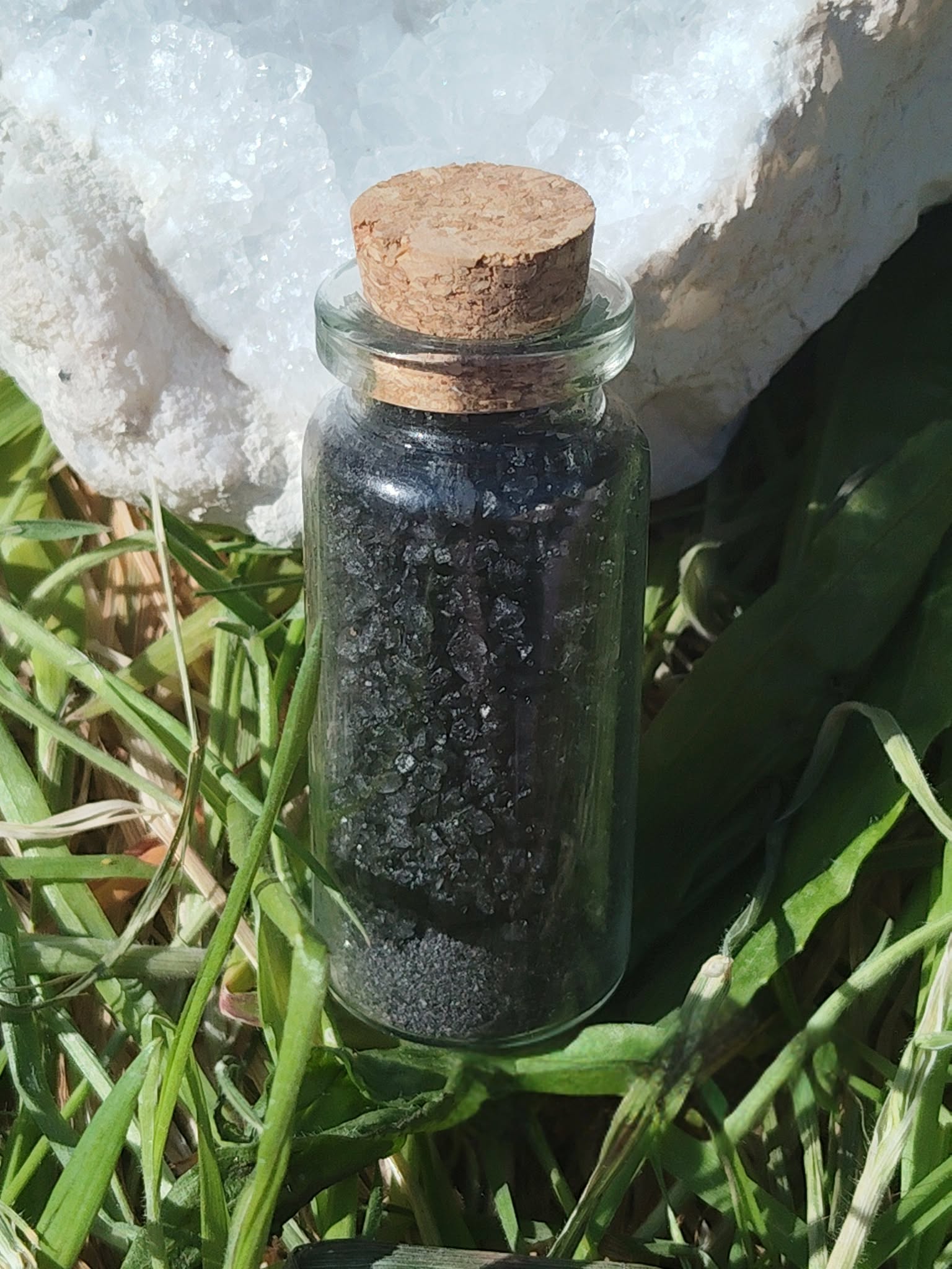 Sel noir ritualisé fait maison Magic Gaïa en flacon verre avec bouchon liège, photo sur herbes et fond clair; usage rituel protection, purification, ancrage, nettoyage énergétique.