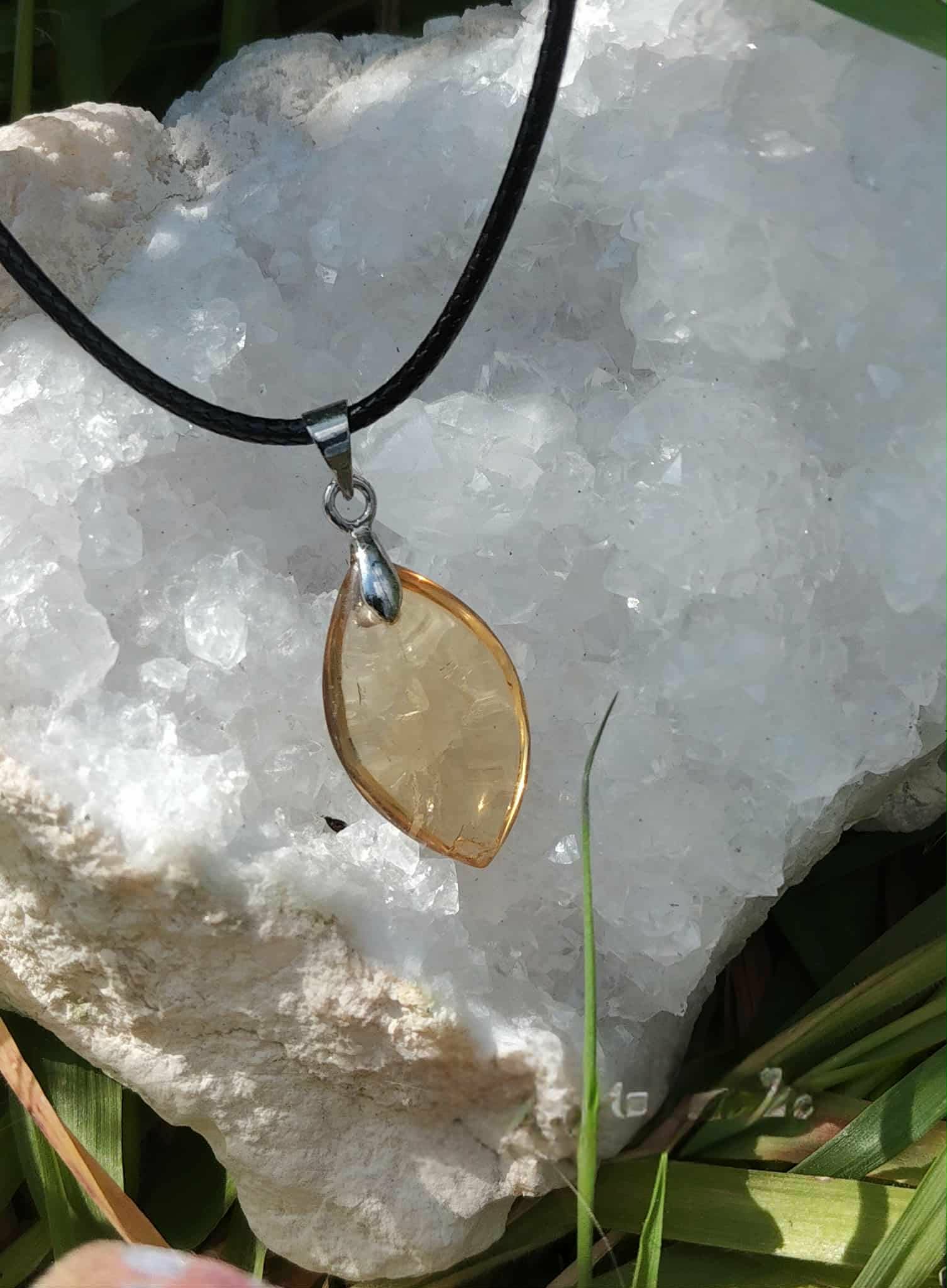 Pendentif citrine sur cordon noir, posé sur amas de quartz blanc en décor naturel, pierre naturelle évoquant la clarté d’esprit, la présence à soi et le dynamisme.
