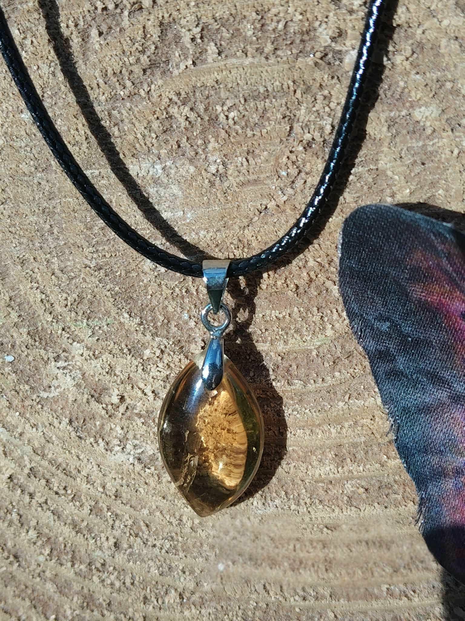 Pendentif citrine sur cordon noir, gros plan sur décor bois clair, pierre naturelle évoquant la volonté, la joie de vivre et la stabilité lumineuse.