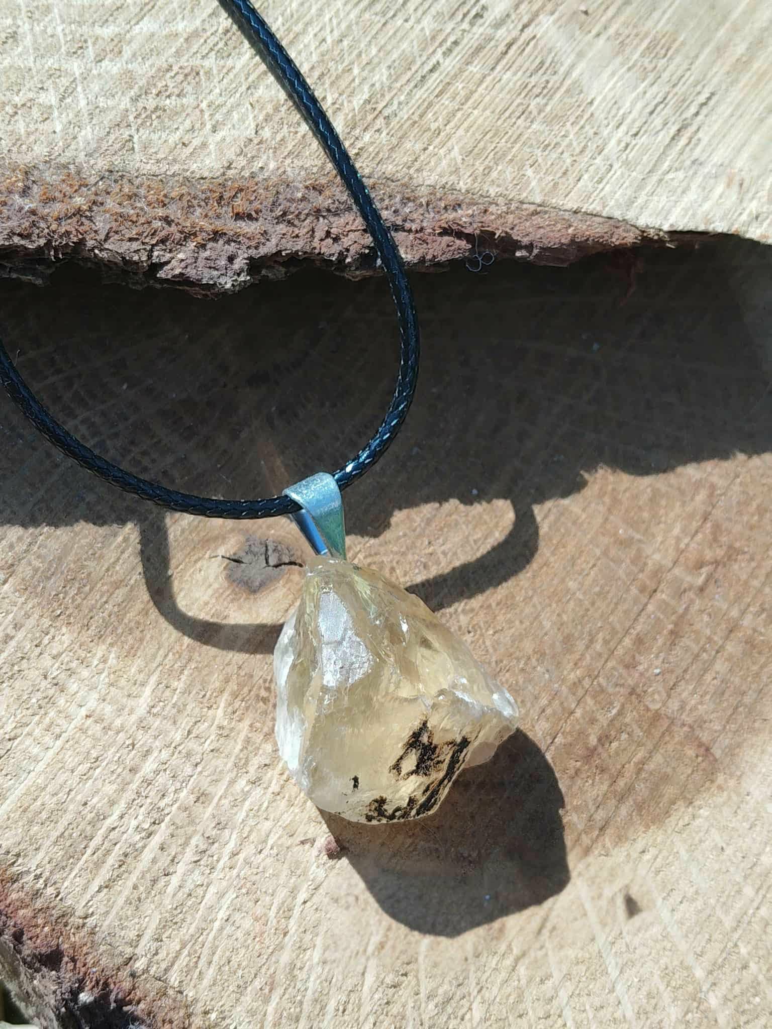 Pendentif citrine brute sur cordon noir, photo sur bois clair en gros plan, pierre naturelle associée à l’élan intérieur, à la chaleur solaire et à la confiance paisible.