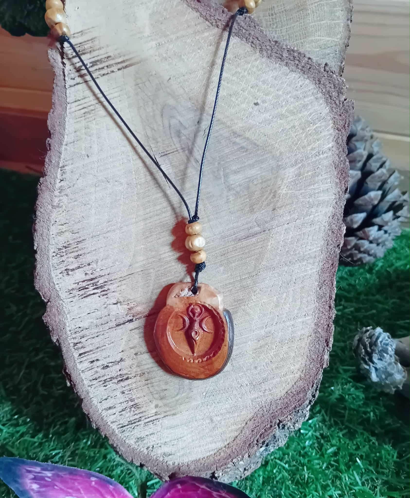 Pendentif en bois Gaïa rond gravé sur cordon noir avec perles bois, posé sur tranche de bois et mousse, symbole Terre-Mère au style nature