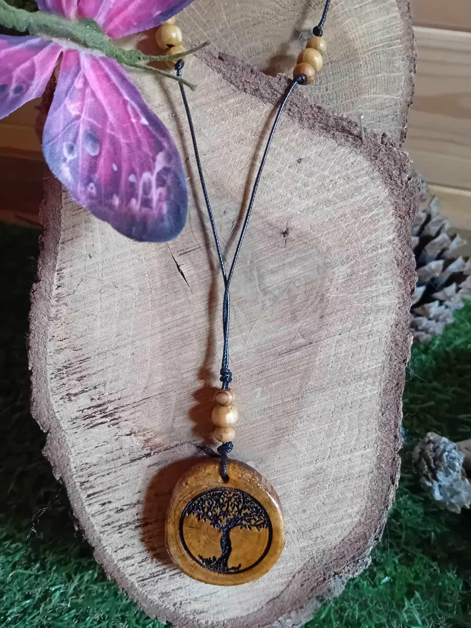 Pendentif Arbre de Vie en bois rond gravé sur cordon noir avec perles bois, posé sur tranche de bois et fleur violette, création nature au symbole d’enracinement