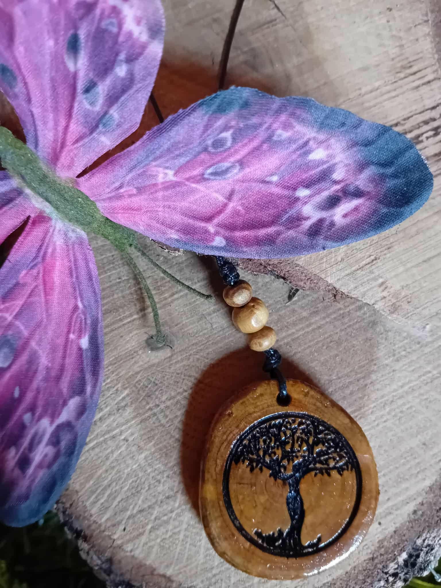 Gros plan sur pendentif Arbre de Vie en bois gravé, cordon noir avec perles bois, décor fleur violette et tranche de bois, esprit terre et croissance