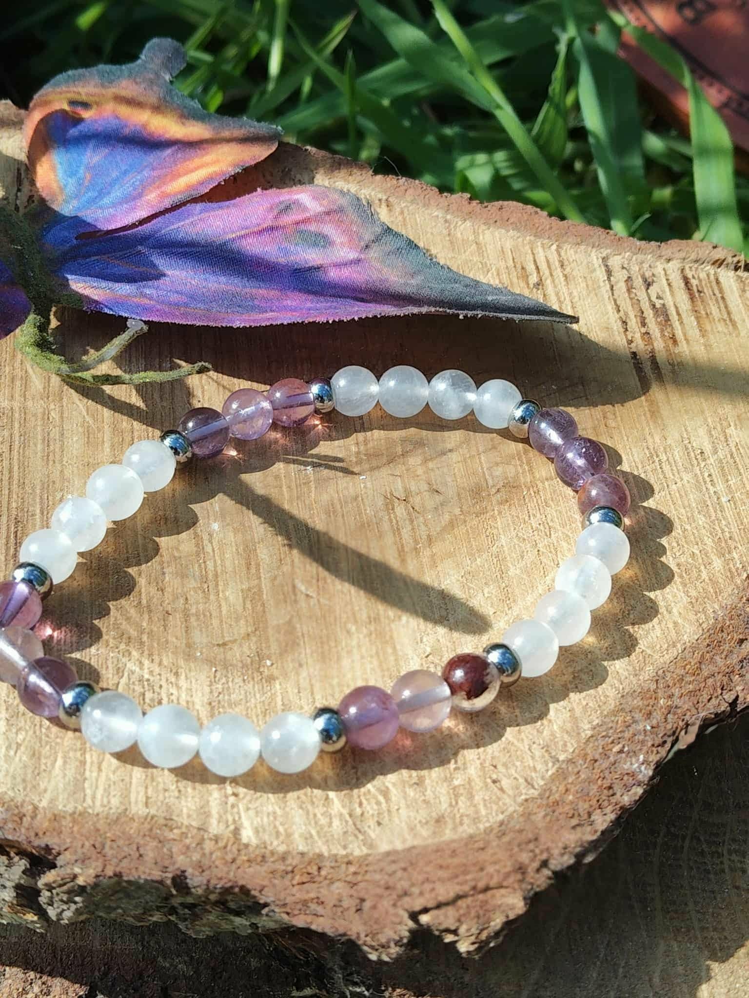 Bracelet lithothérapie clairvoyance sur tranche de bois avec papillon violet et herbe, perles blanches et violettes, apaisement et perception subtile