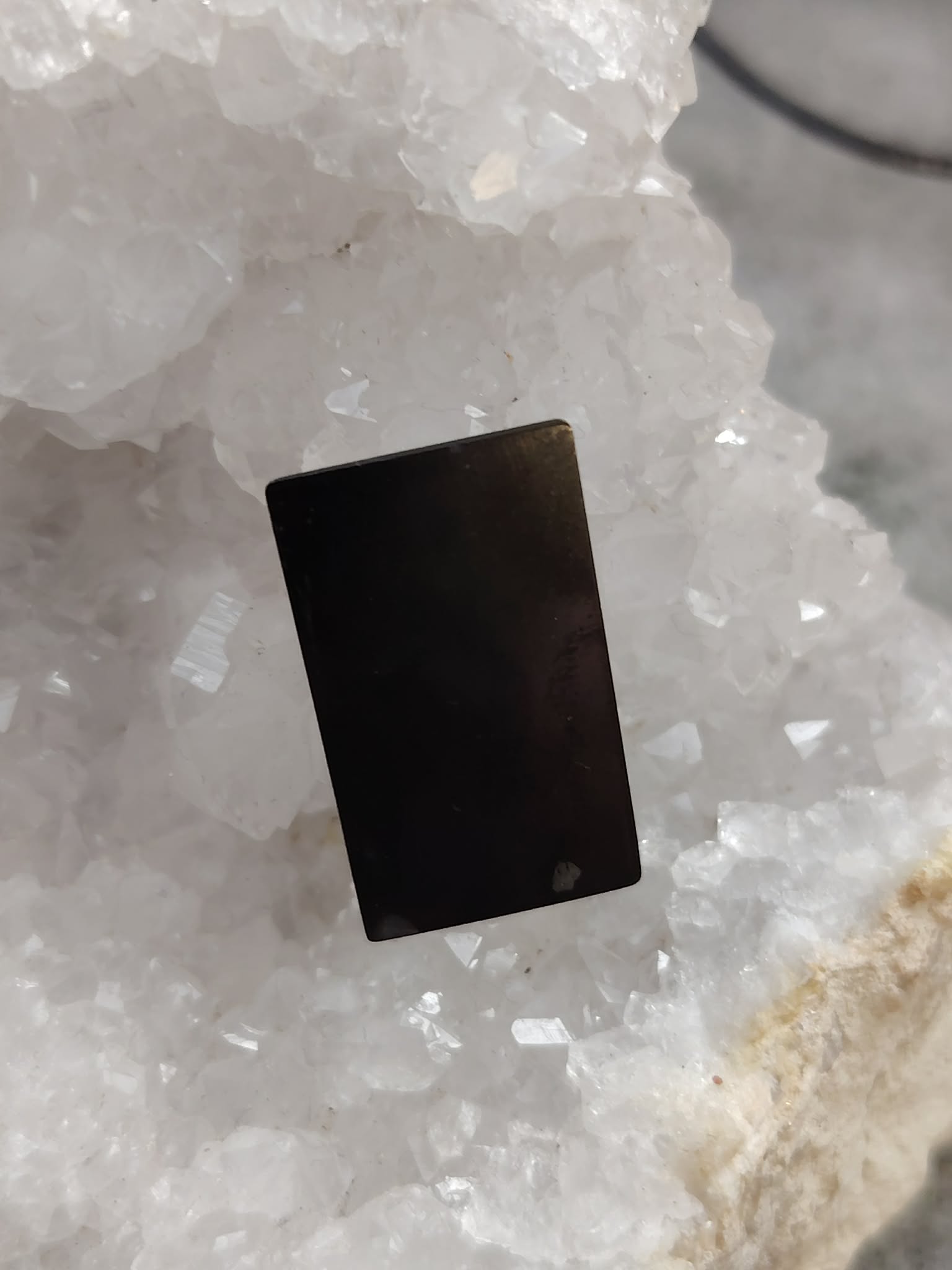 Plaque de shungite adhésive pour téléphone (anti-ondes) posée sur amas de quartz blanc, photo produit Magic Gaïa, vertus variées : protection énergétique, ancrage, recentrage, apaisement.