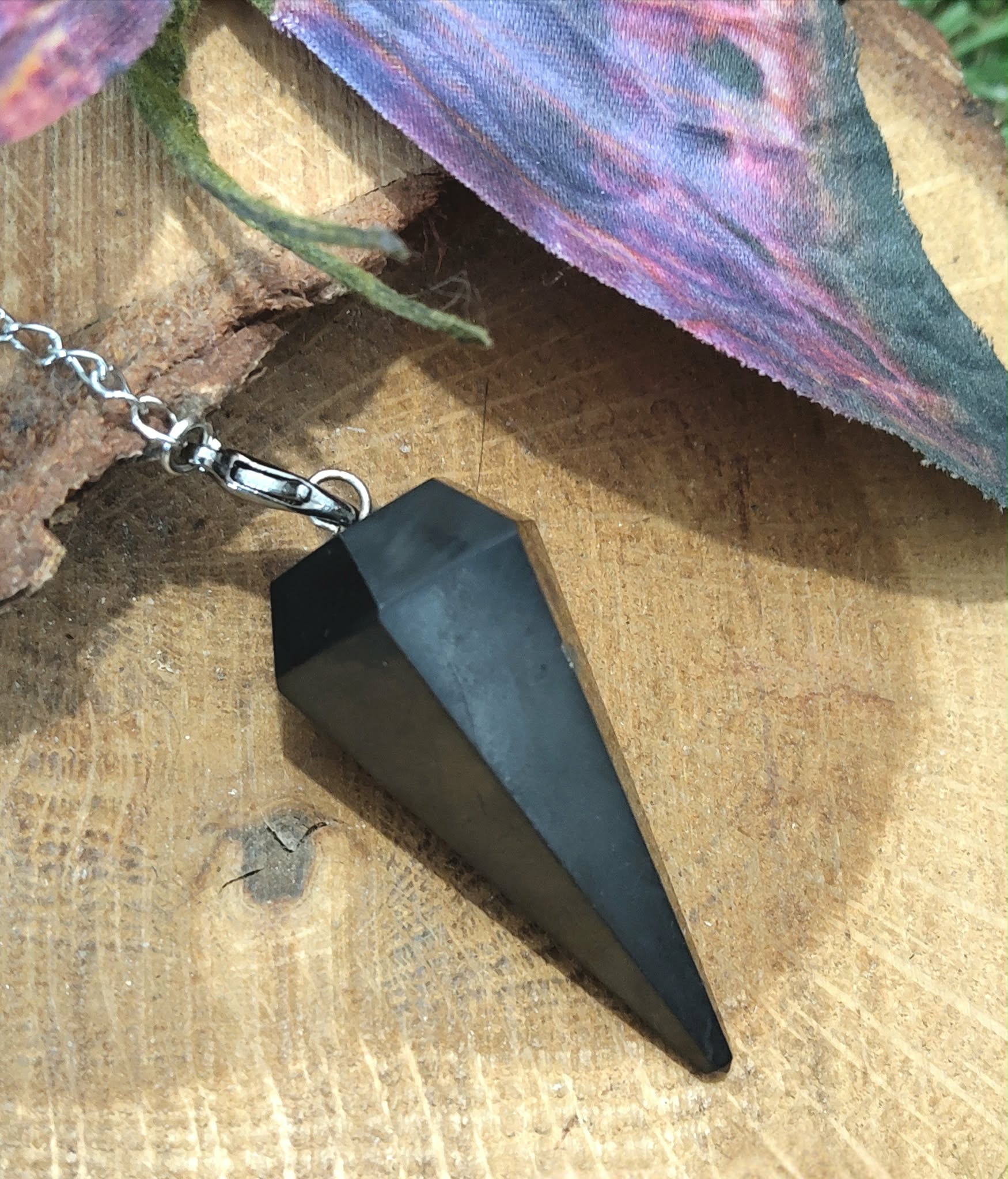 Pendule en shungite noire sur rondin de bois, décor naturel witchy, chaîne argentée, radiesthésie/divination, ancrage, protection, purification, clarté mentale, apaisement • Magic Gaïa