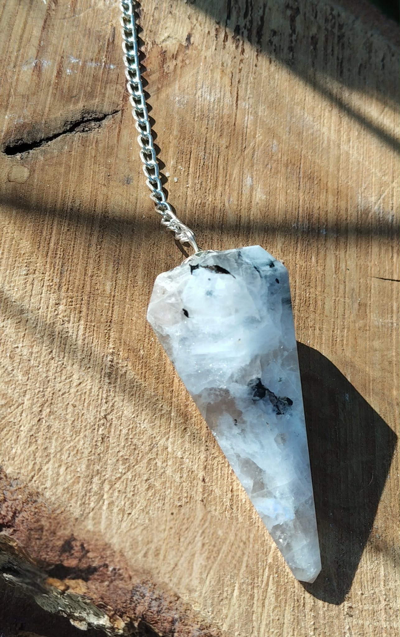 Pendule en péristérite (pierre de lune) facettée personnalisable sur demande, chaîne argentée, posé sur rondin de bois, décor naturel, radiesthésie/divination, intuition, apaisement, clarté, protection douce, équilibre émotionnel • Magic Gaïa