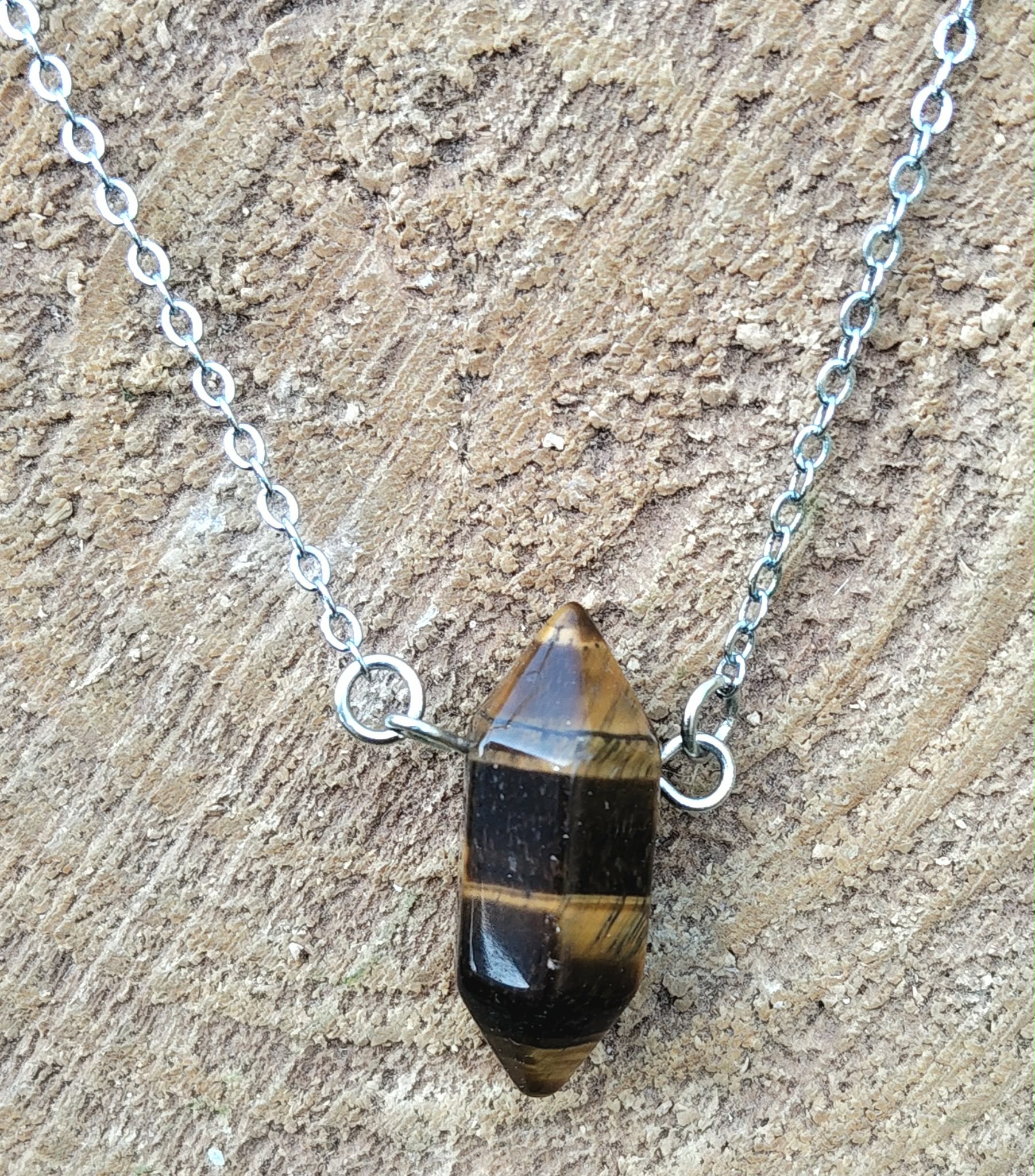 Pendentif pointe œil de tigre sur chaîne en acier inoxydable, photo sur fond bois clair texturé, pierre naturelle associée à la lucidité, à l’aplomb et à la présence à soi.
