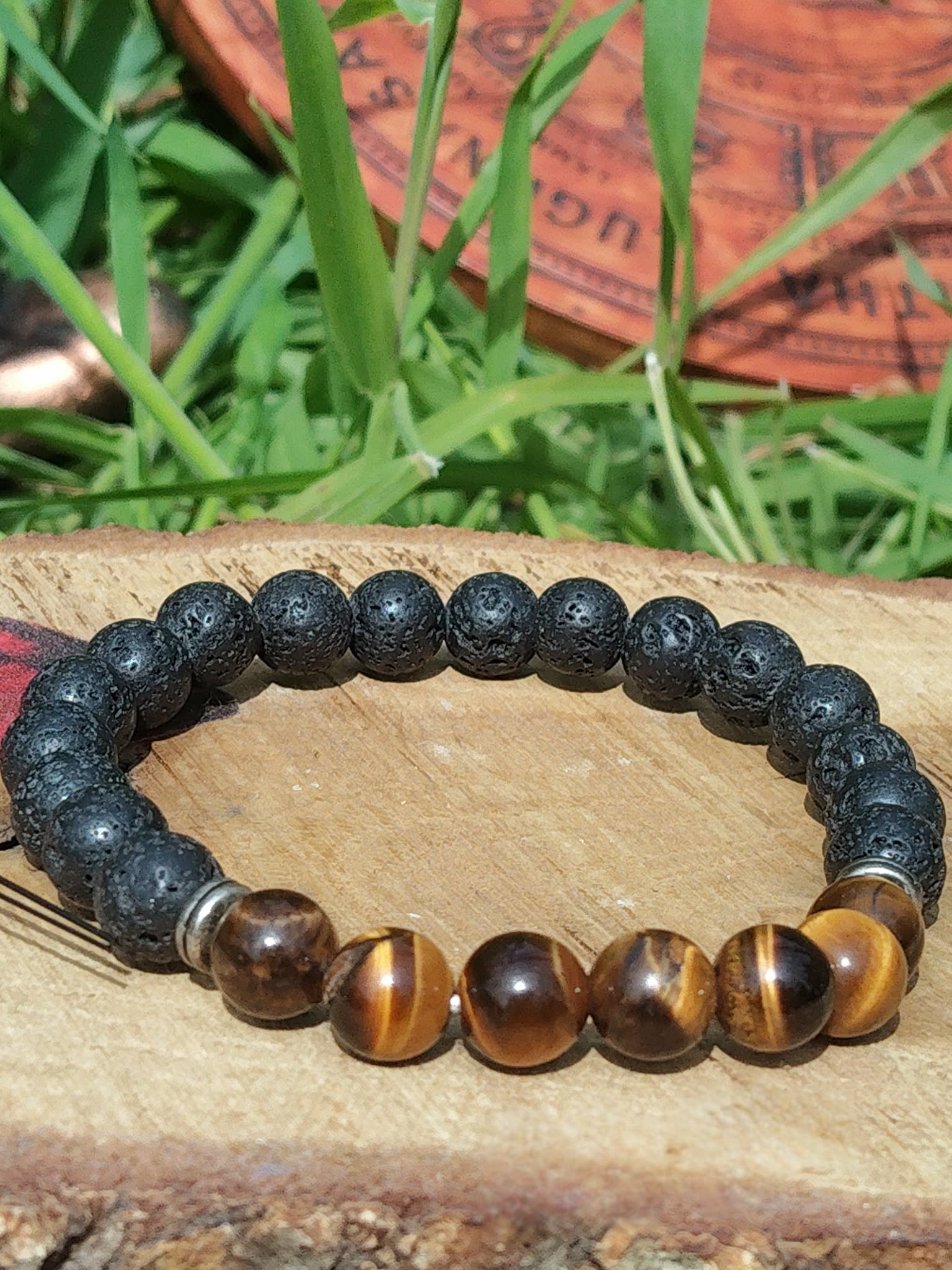 alt="Bracelet œil de tigre et pierre de lave 8 mm sur élastique, décor bois et herbes, protection, ancrage, assurance