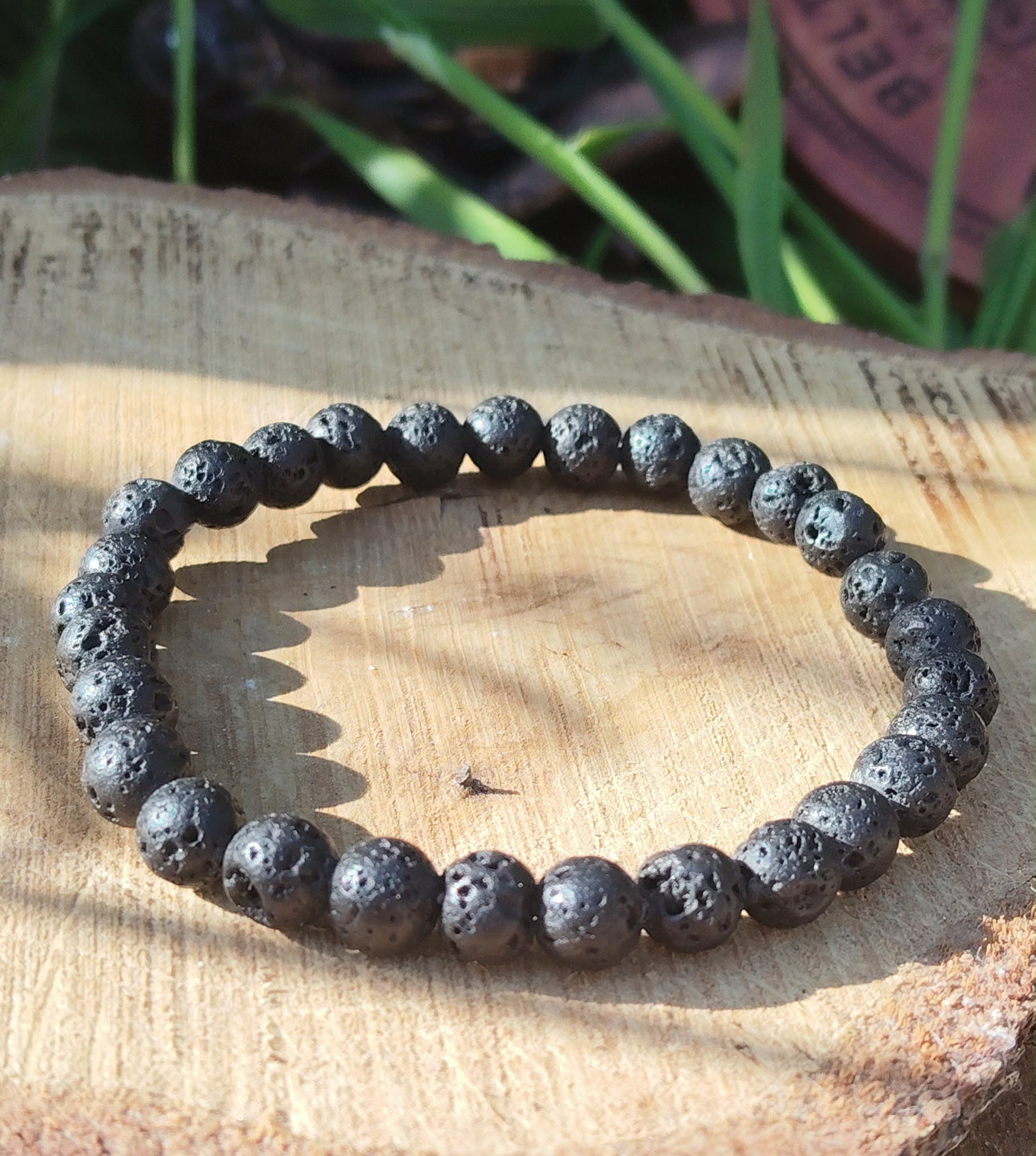 Bracelet Pierre de Lave 6 mm sur élastique, perles noires poreuses sur tranche de bois avec herbes, ancrage et force intérieure.
