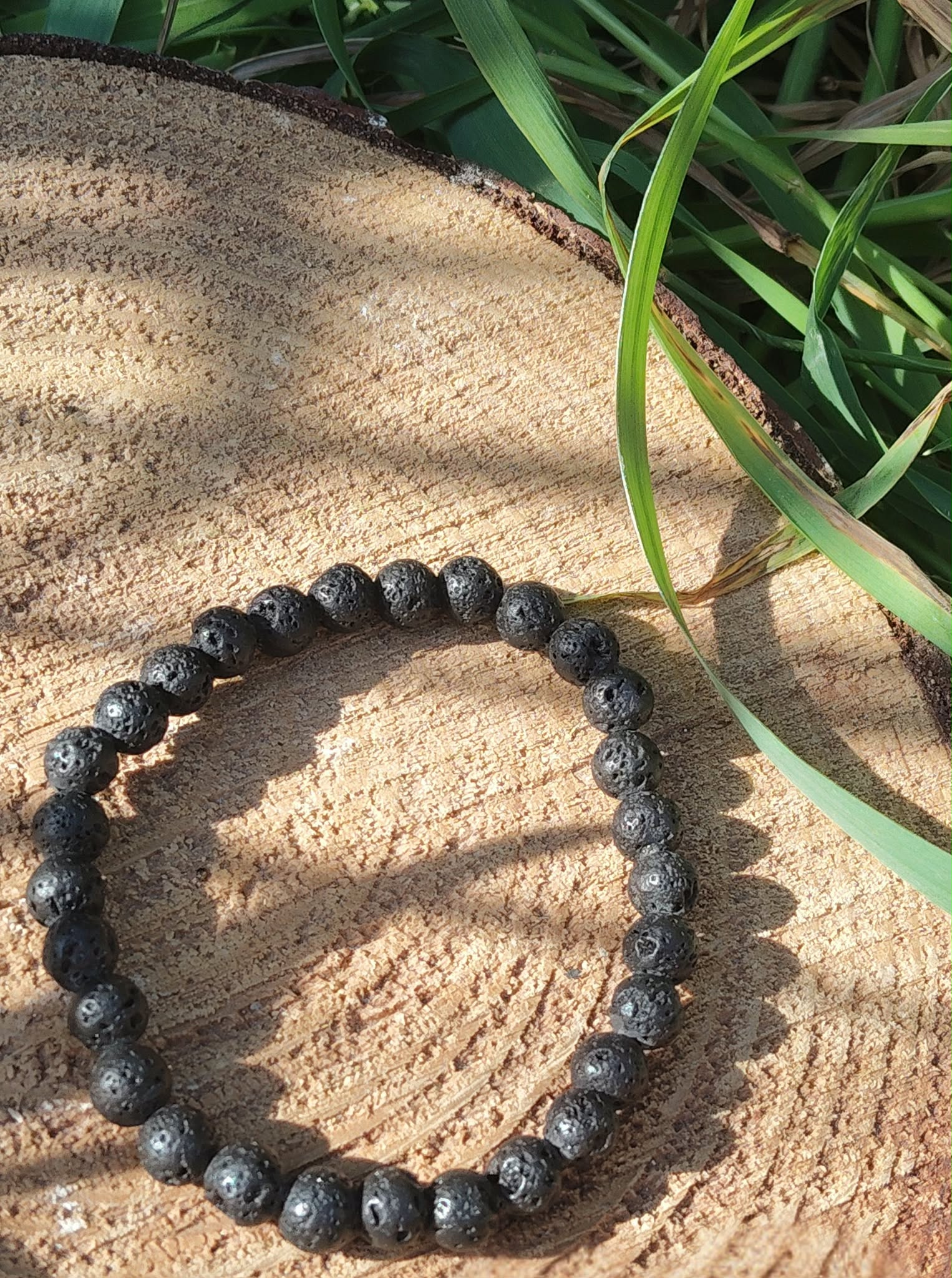 Bracelet Pierre de Lave 6 mm sur tranche de bois avec herbes et ombres douces, énergie stable, force calme et ancrage.