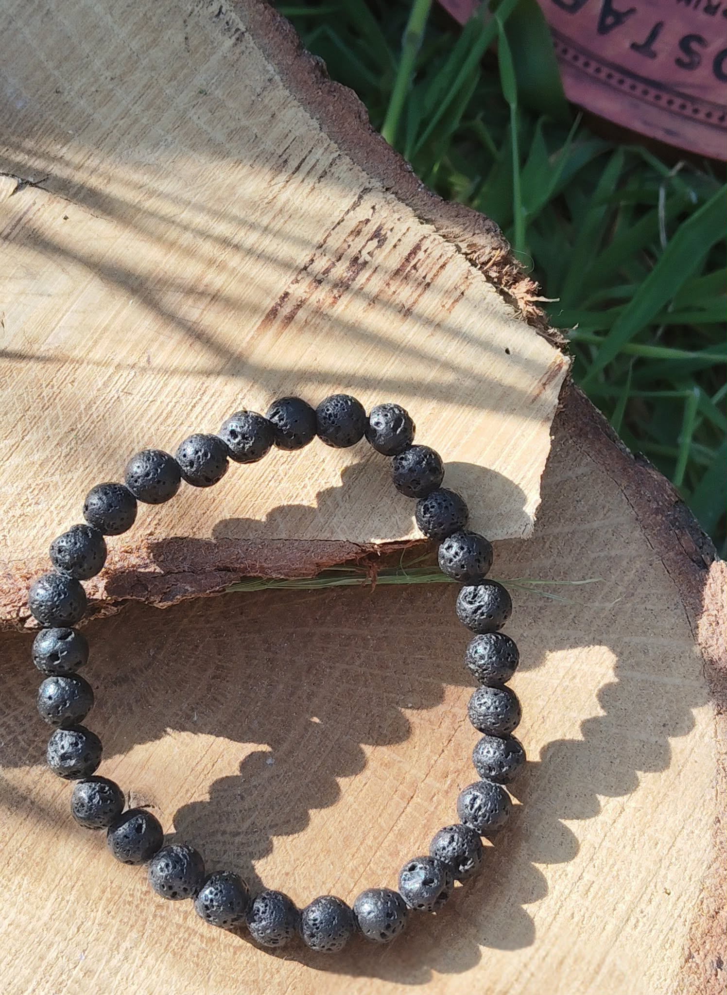 Bracelet en pierre volcanique 6 mm sur fond bois et herbes, perles de basalte noires, persévérance, stabilité et apaisement mental.