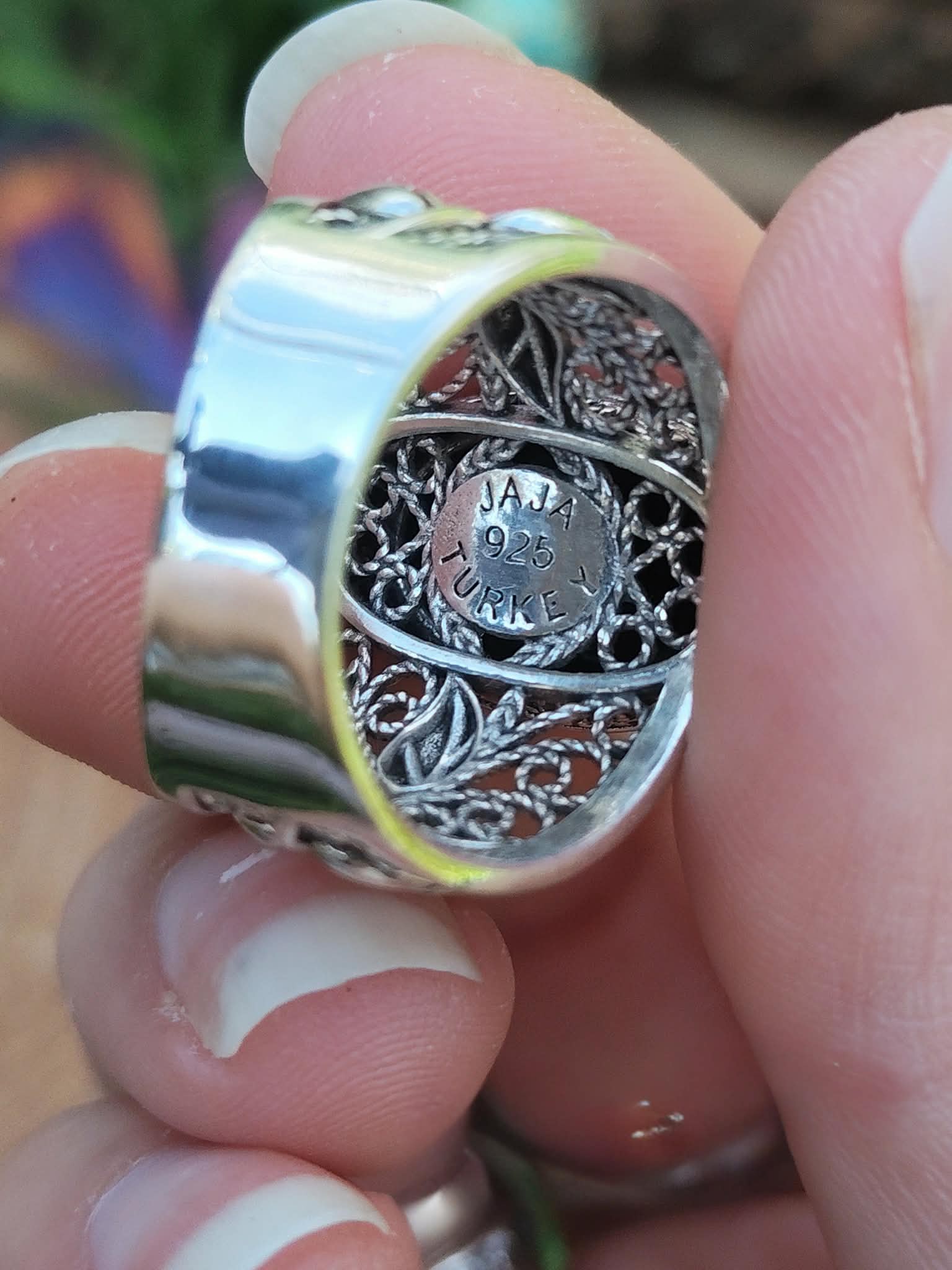 Bague argent 925 large anneau filigrane vue arrière tenue entre les doigts fond flou multicolore intentions associées protection ancrage stabilité force intérieure