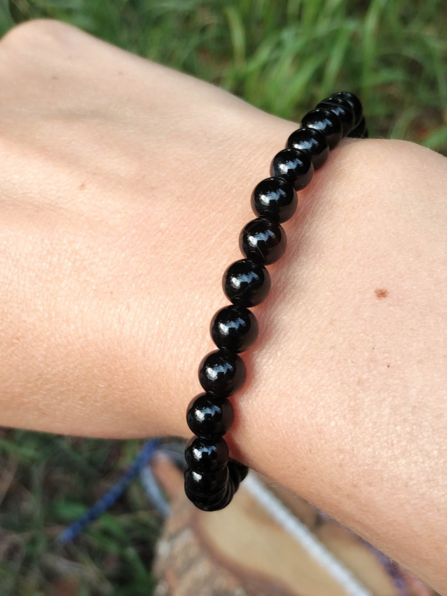Bracelet Onyx noir en perles rondes brillantes porté au poignet en extérieur, retenue, assurance et limites émotionnelles.