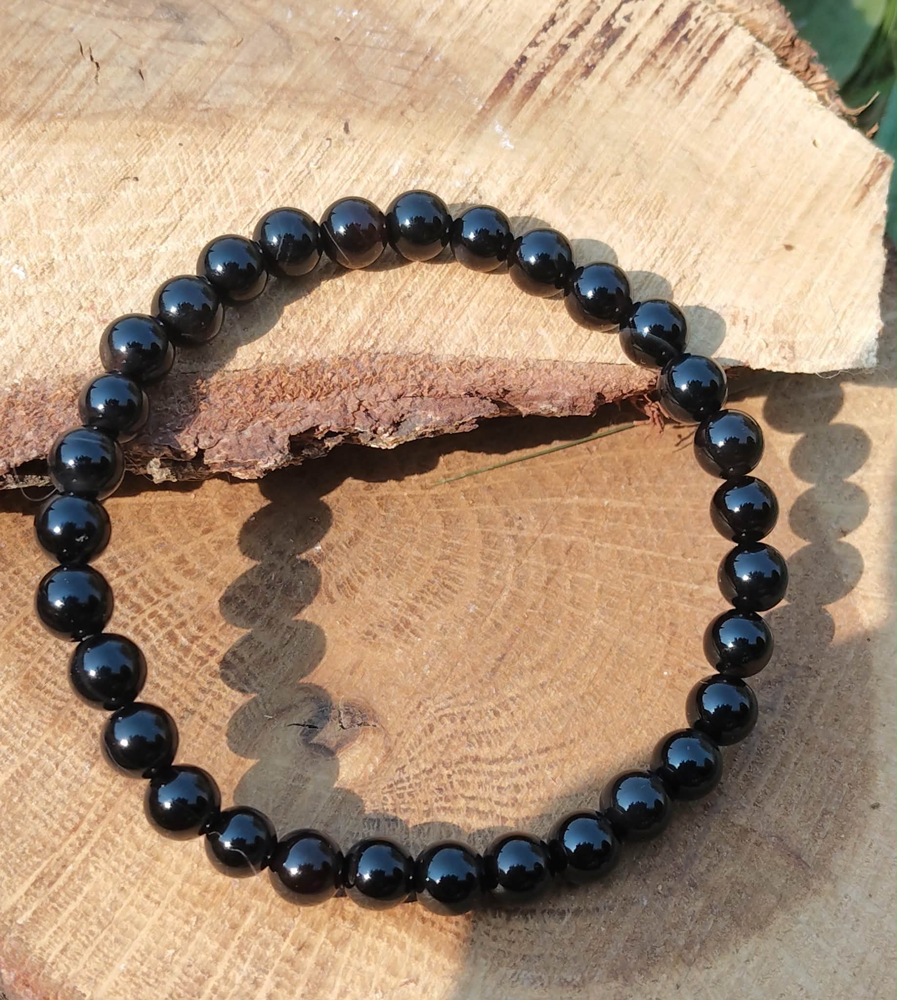 Bracelet Onyx noir en perles rondes sur tranche de bois texturée, ombre visible, concentration, structure et maîtrise intérieure.